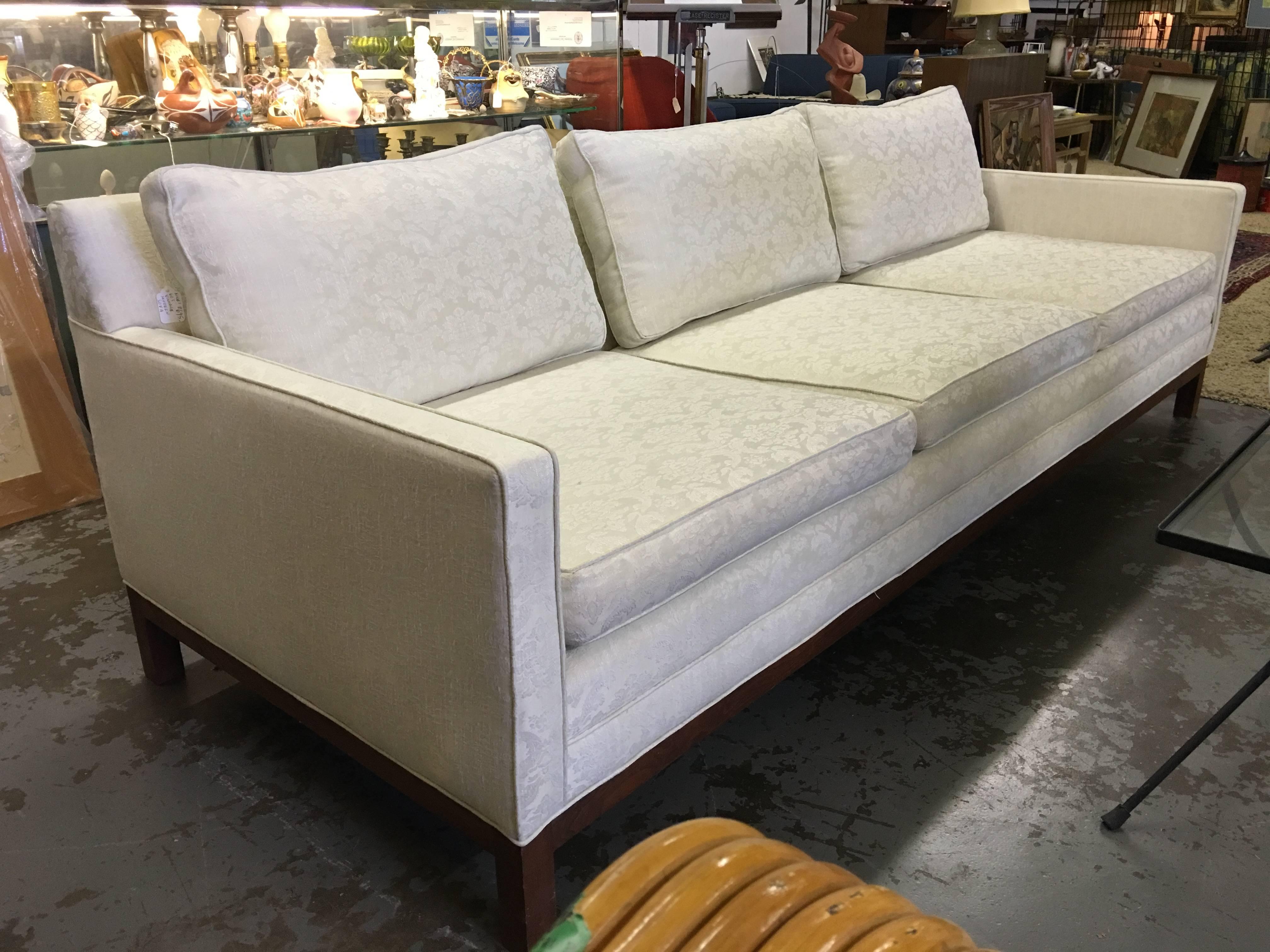 This is a very nice low sleek scale sofa designed by Milo Baughman for Dillingham. It rests on a walnut bracket base. It is done in a fanch tone on tone off-white damask material, you will need to redo. It has several light spots, not too bad. It is