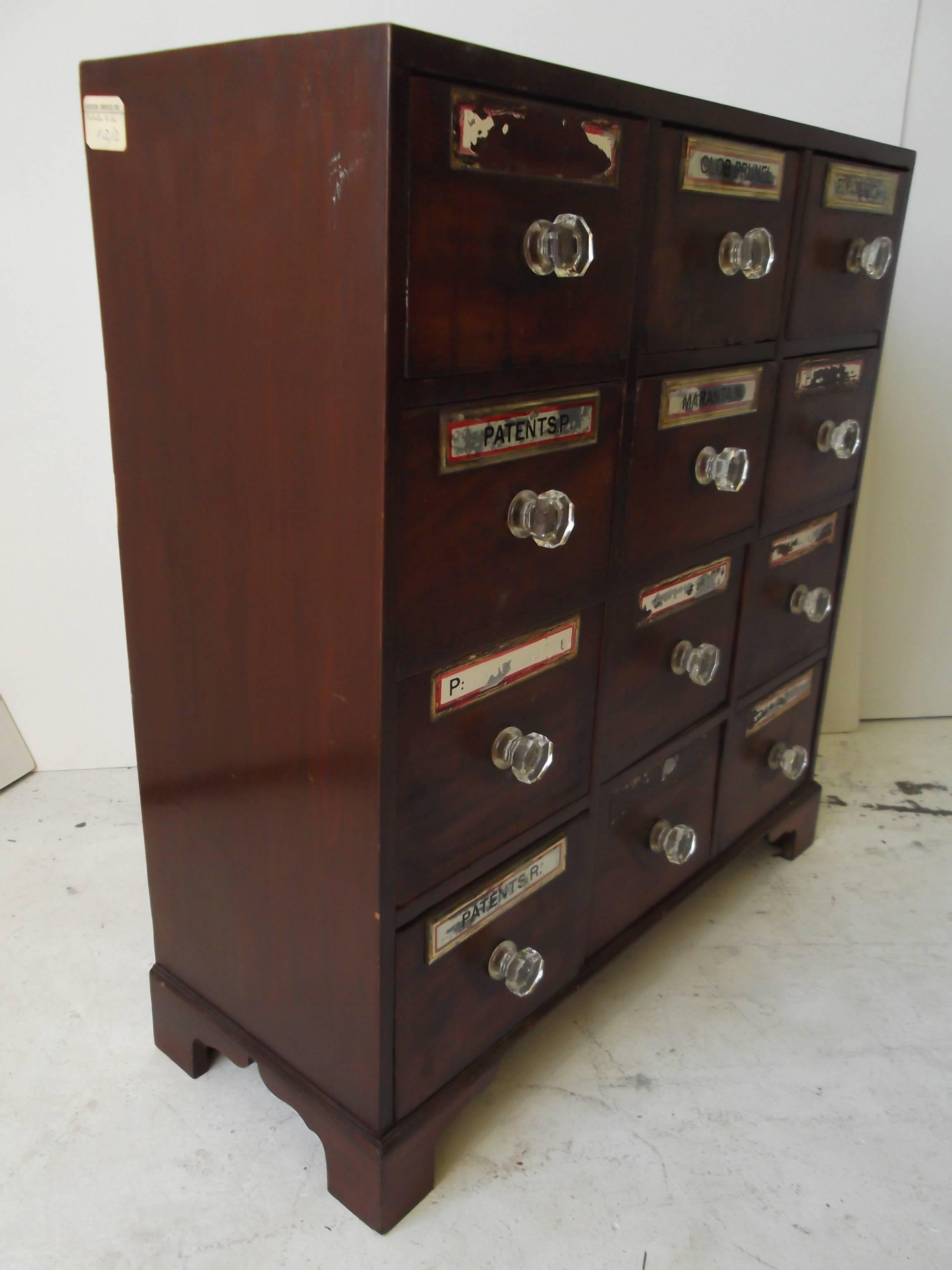 This is a wonderful smaller antique apothecary chest with 12 drawers. It is in mahogany, circa 1850. It retains glass knobs and several of the reverse painted mirror labels. It is believed to be English in origin. The construction is nice, with old