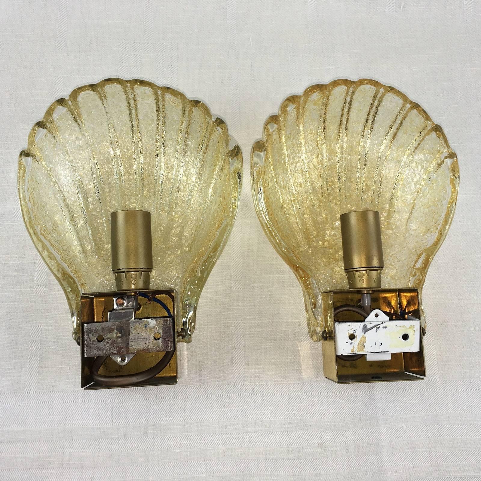 A pair of 1960s sea shell form sconces, produced in Italy, in textured glass, with tones of gold, affixed against a polished brass base. Each Fixture requires one European E14 candelabra bulb, each bulb up to 40 watts.