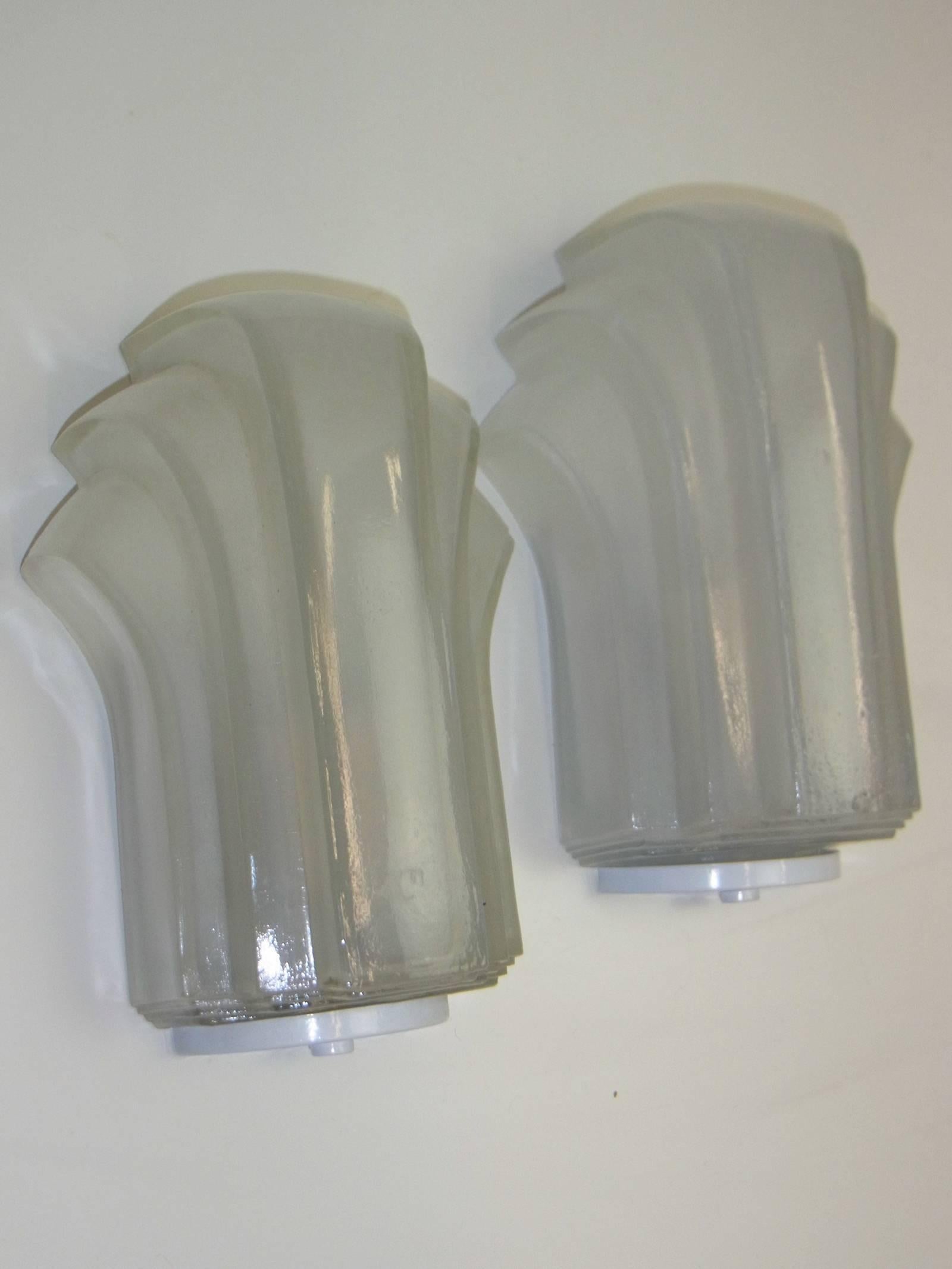 One pair of Art Deco style sconces. These Art Deco style wall sconces feature an enamel white mounting with a multi-tiered, Skyscraper style design. The frosted relief glass shades rest atop the frames for a seamless design. Each fixture requires