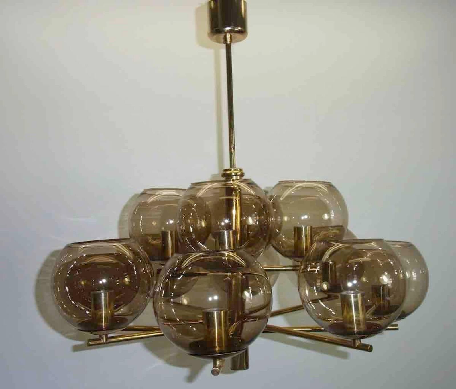A twelve-light chandelier in its original brass finish with amber globe glass shades designed by Hans-Agne Jakobsson.
 
Fixture requires twelve European E14 candelabra bulb each up to 40 watt. 

Due to the vintage nature of this fixture, there