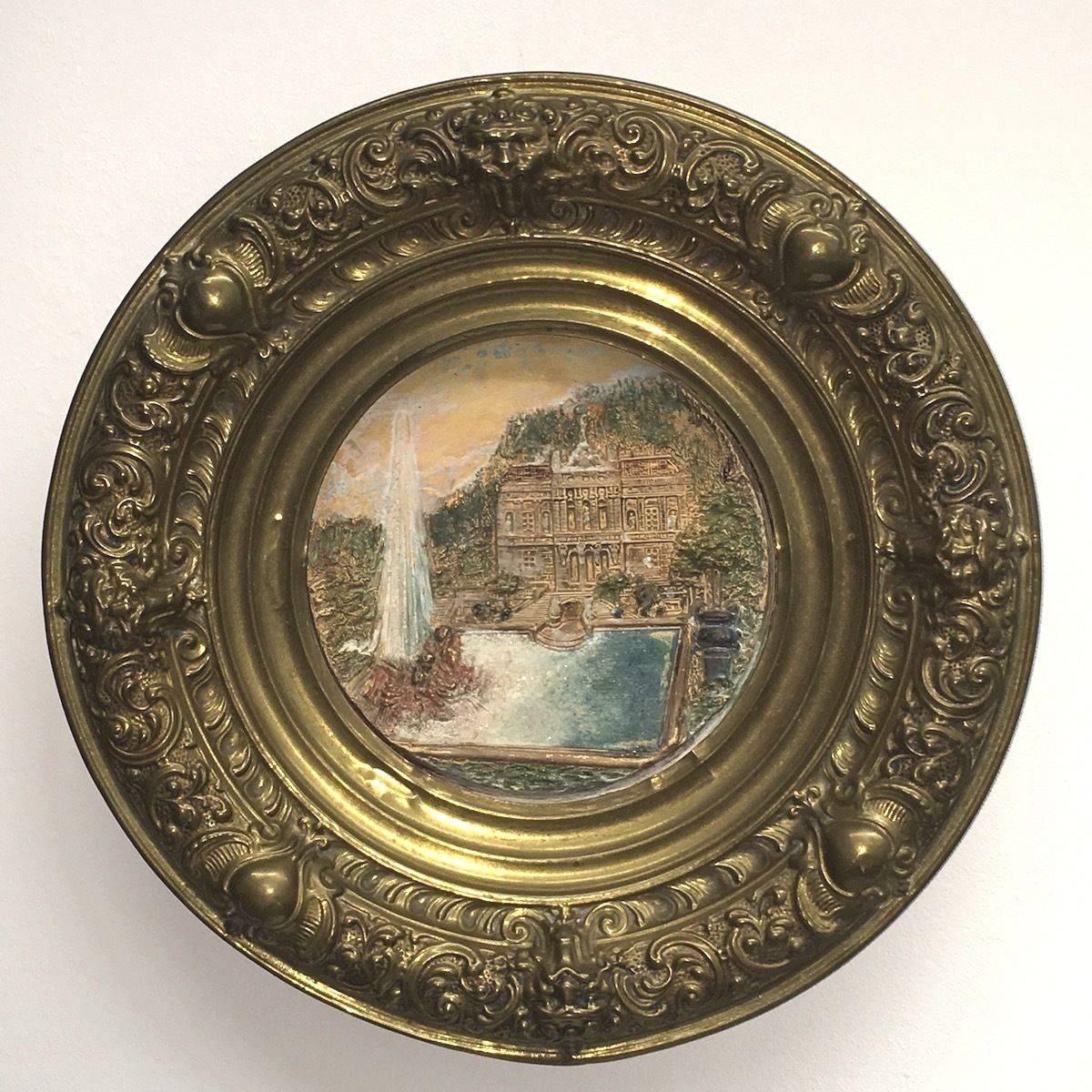 A large German faience plate framed by brass, circa 1880. The faience plate represent castle Linderhof in a landscape. The brass is entirely decorated with flowers, hearts and lions.
Very elegant reflection of the era  and a lovely display of King