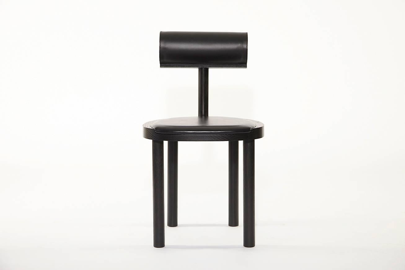 Chaise de salle à manger UNA en chêne teinté noir, recouverte de cuir. L'utilisation de ces formes fluides permet de mettre davantage l'accent sur les détails du grain du bois et du dessus en cuir cousu à la perfection.

Fabriqué en chêne massif,