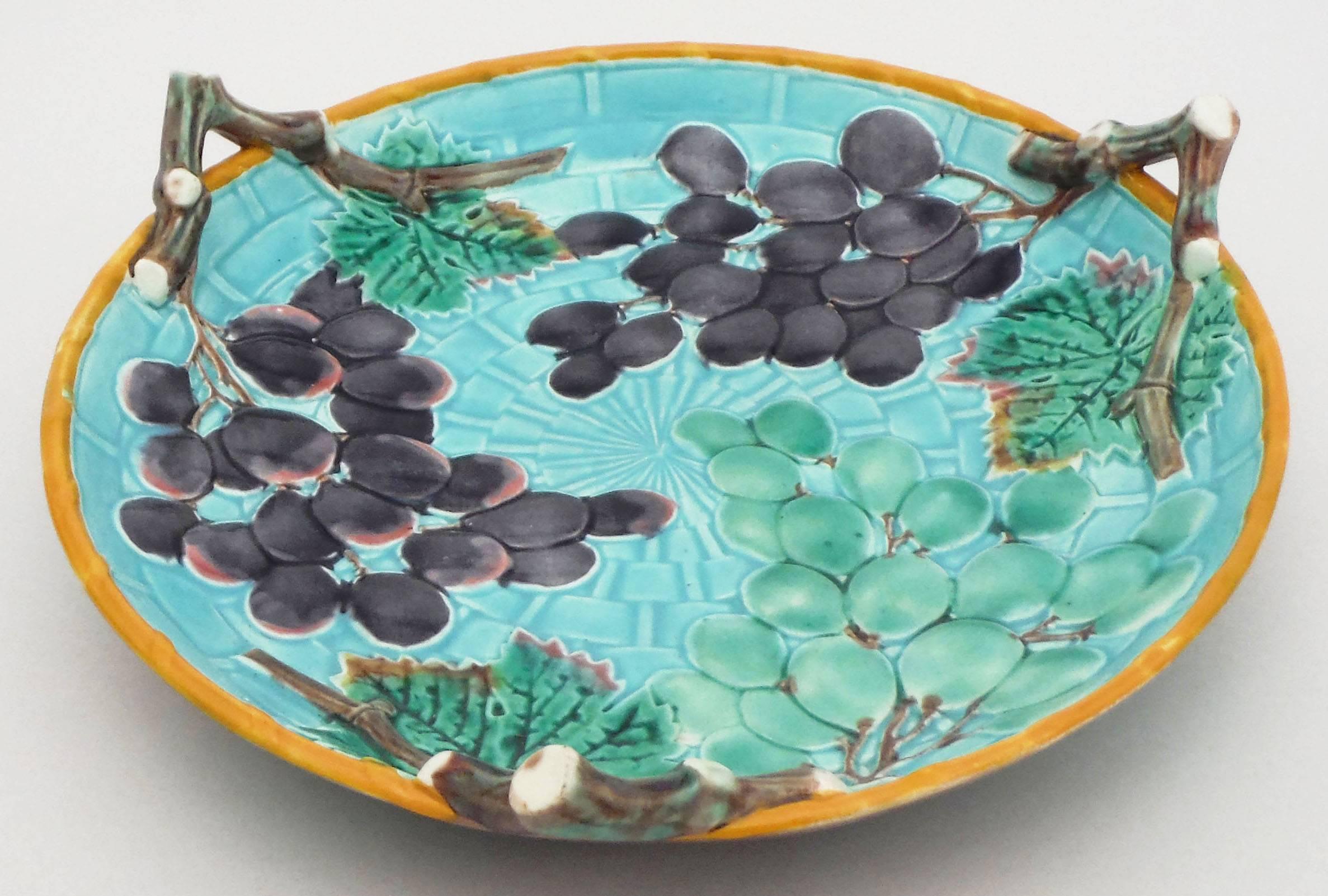 Colorful and lovely turquoise Majolica handled platter with grapes signed Wedgwood.
The three handles are branches, the background is a aqua basketweave with a thin yellow border.