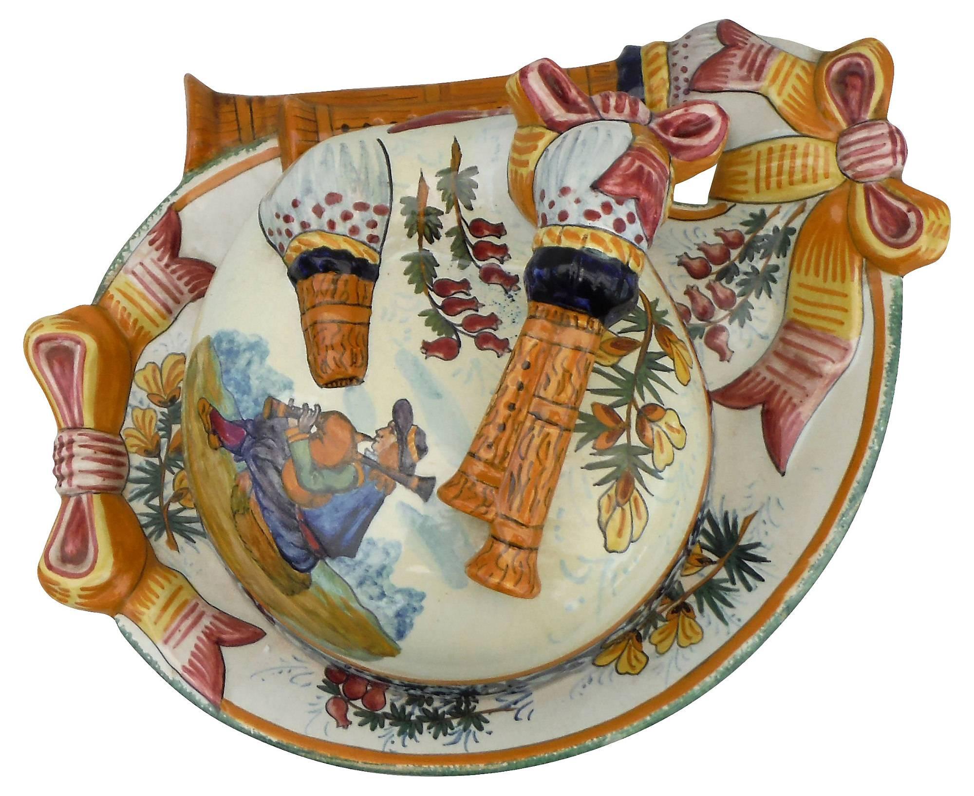 Charming large French butter dish with a breton playing bagpipe , the butter dish have also a bagpipe shape , the piece is decorated with flowers and bows signed Henriot Quimper, circa 1920.