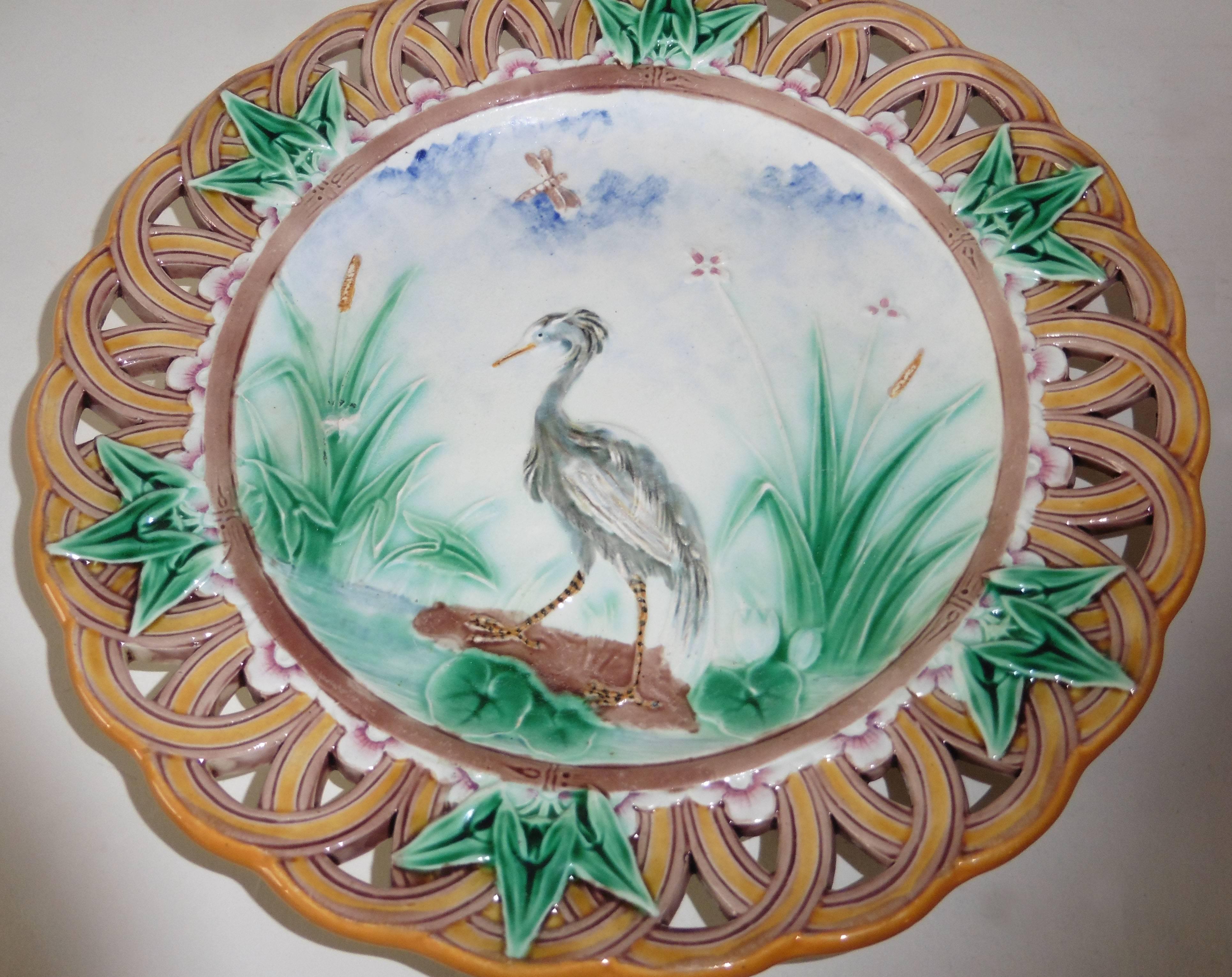 Une fine assiette réticulée en majolique victorienne signée Wedgwood.
La bordure est décorée de feuilles de lierre, le centre est un paysage avec un héron près d'un étang.