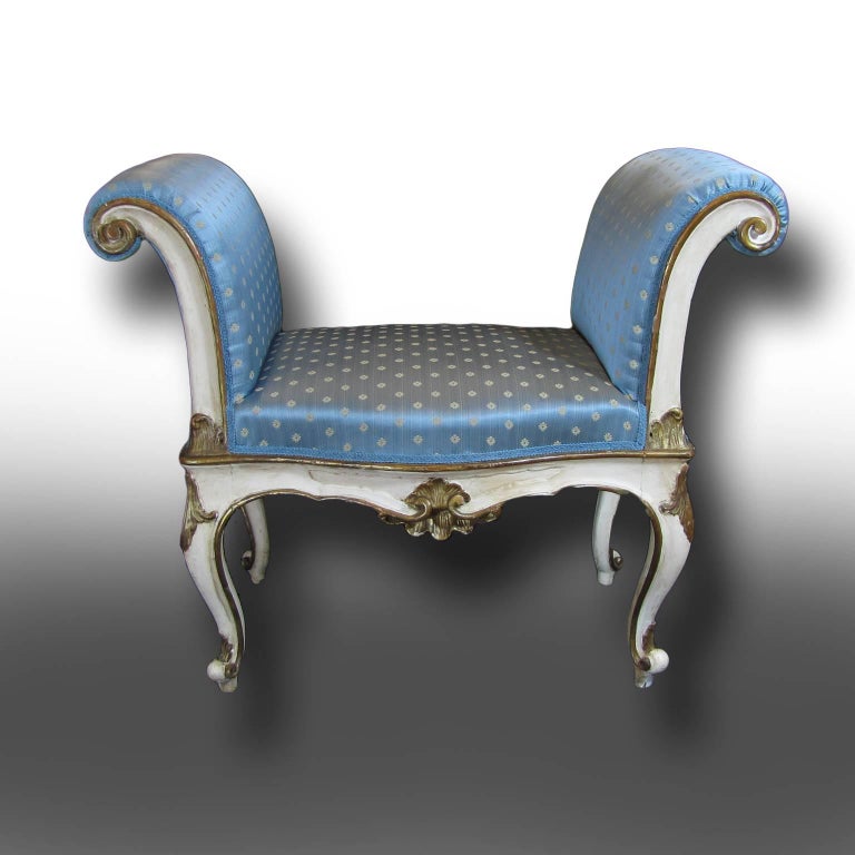 This benches are made of solid finely carved solid wood and are finished in white Tempera Magra and golden paint details. The four slender capriole legs are surmounted by the finely carved seat and arms, which are completely upholstered in a light
