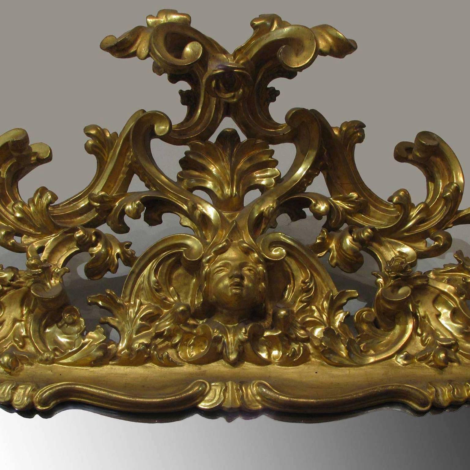 
A monumental Tuscan mirror in a carved and leaf gilded wooden frame with floral scrolls, figures, cherubs, gargoyles and silvered mirror plate.
Made in the first half of the 18th century, during the period of Louis XV. 
For its features, as the