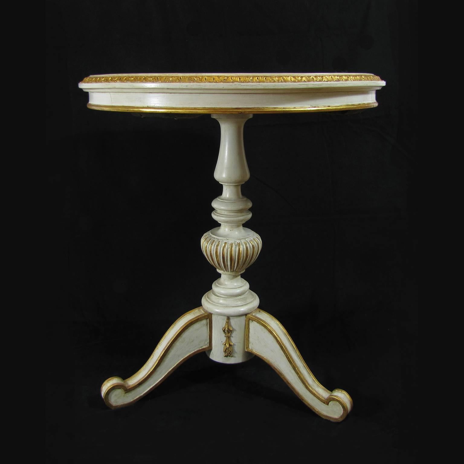 A centre table in carved wood, painted with white tempera magra, some golden painted details and a Pietra Dura tabletop.
One vertical vase-shaped leg with tripartite base is surmounted by a built-in marble tabletop in Belgian black marble and an