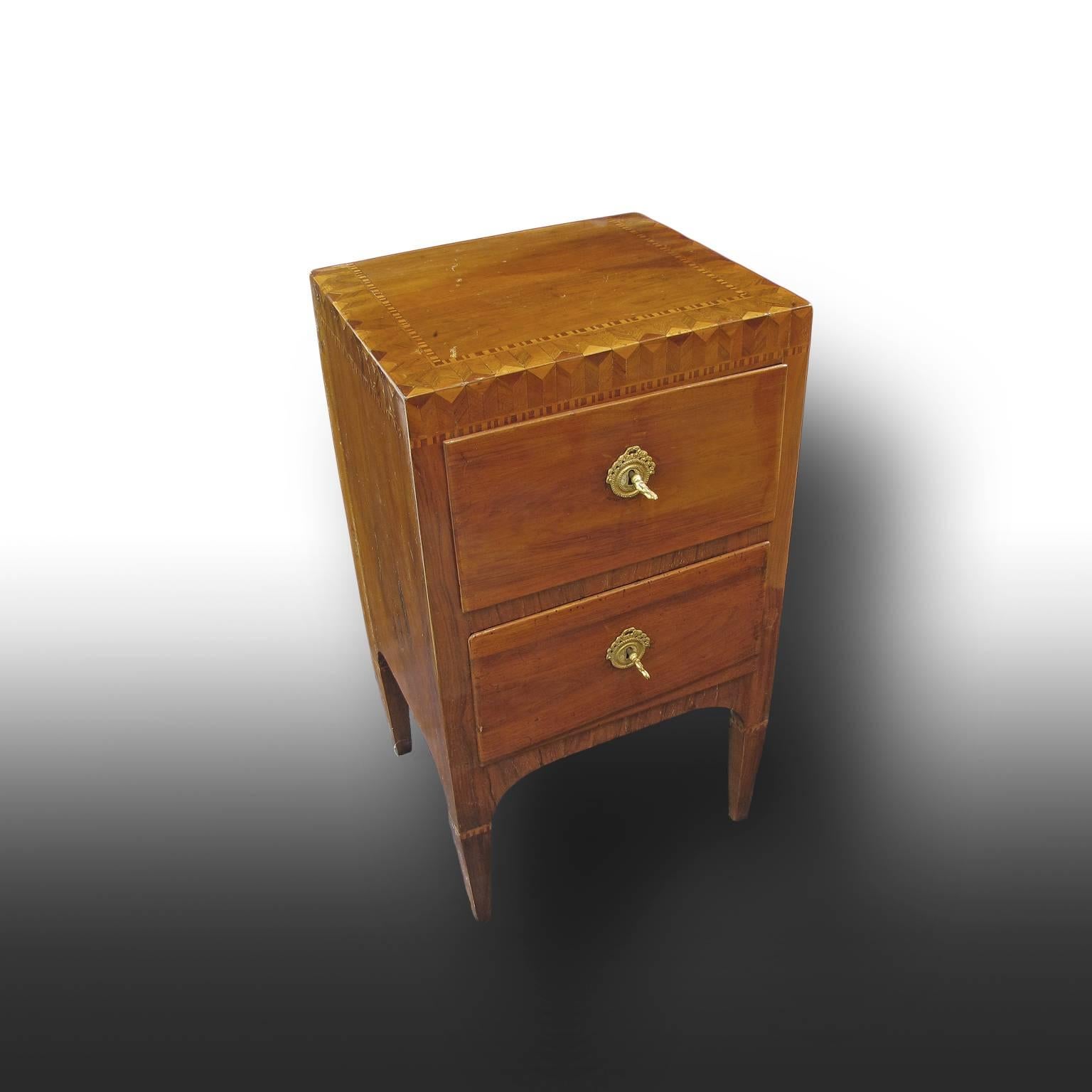 A pair of small solid walnut wood bedside tables or nightstands with a very fine inlay in olive and cherrywood along the top edges. 
The pieces of furniture are supported by four inverted pyramid trunk legs and do have two drawers each. 
The