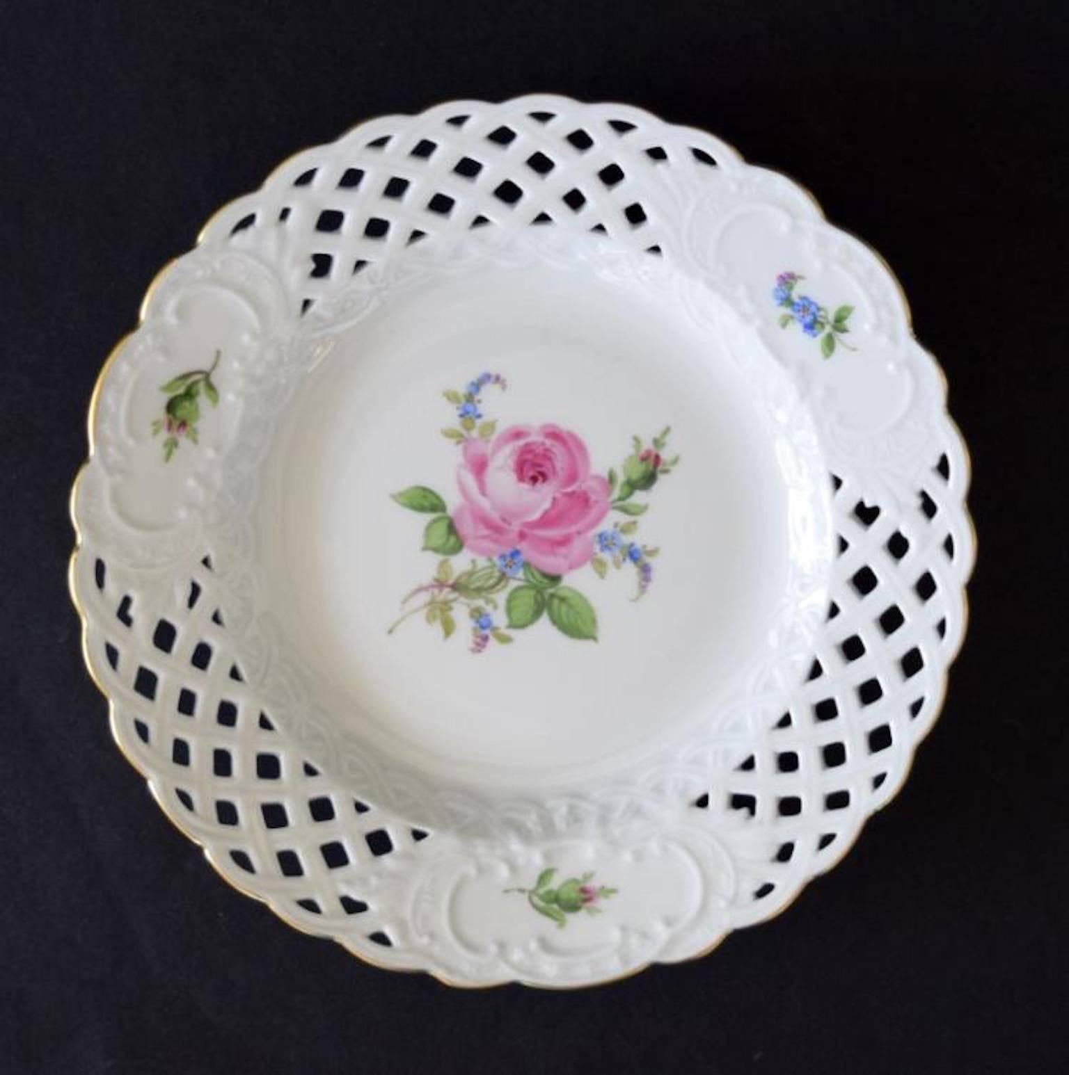 This gilt-rimmed plate features a central pink rose design surrounded with rosebuds and small blue flowers. This piece of porcelain was made by Meissen in a reticulated or woven pattern and is marked 020810 on the base. It is 6" in diameter.