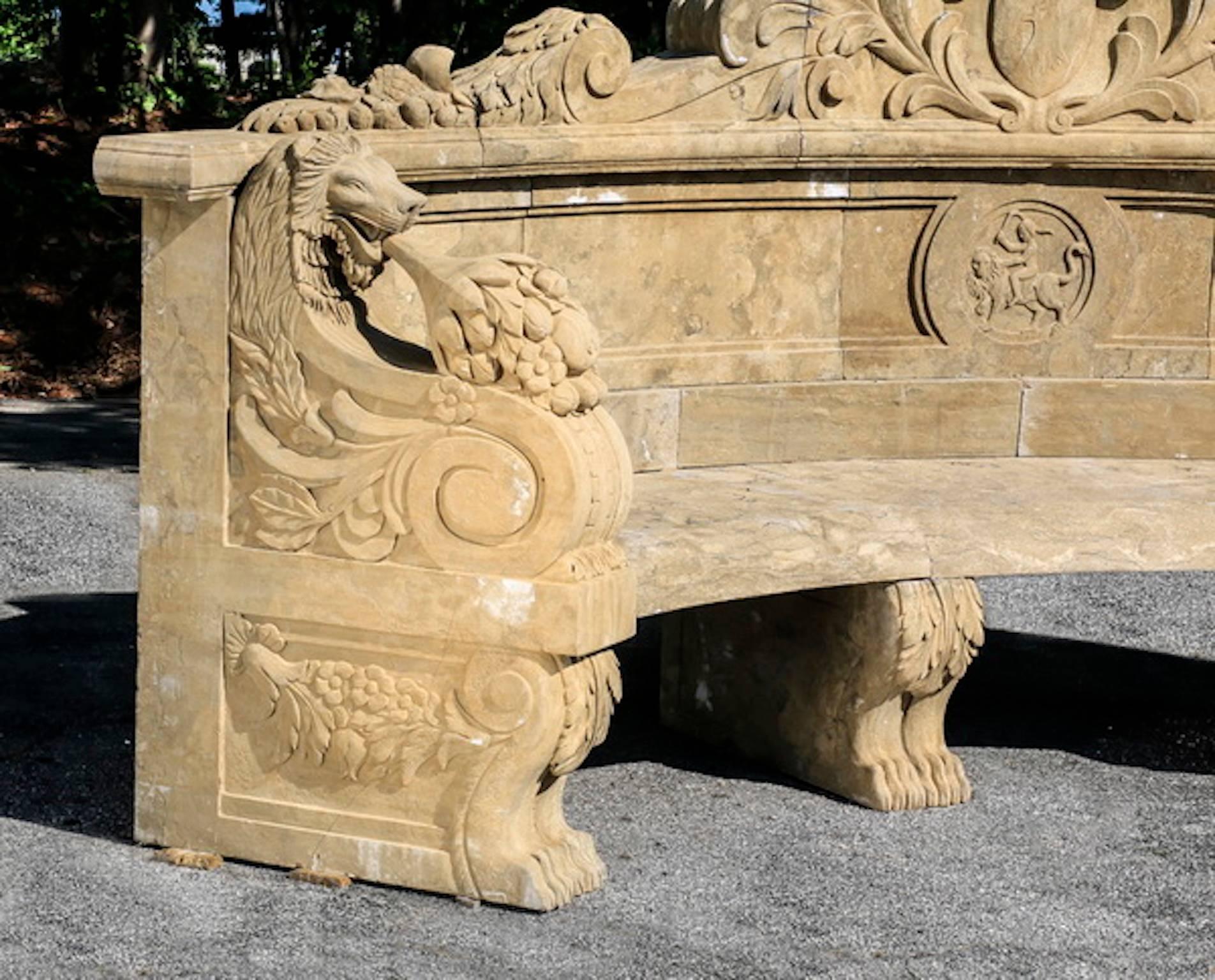 Carved marble garden bench in the Neoclassical taste, the demilune bench with carved backrest and elaborate winged lion armrests, surmounted by the carved pediment with a shield crest flanked by scroll work, the whole rising on four figural lion's