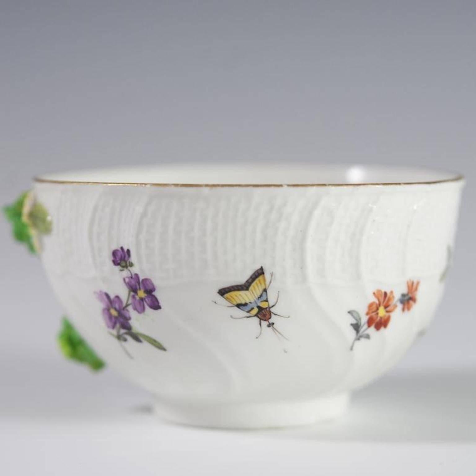 An antique Meissen demitasse cup. Features hand-painted decoration of ants and butterflies along with floral motif. Finished with molded porcelain flowers, wicker basket textured border, and gilded trim and accents. Marked on bottom with blue