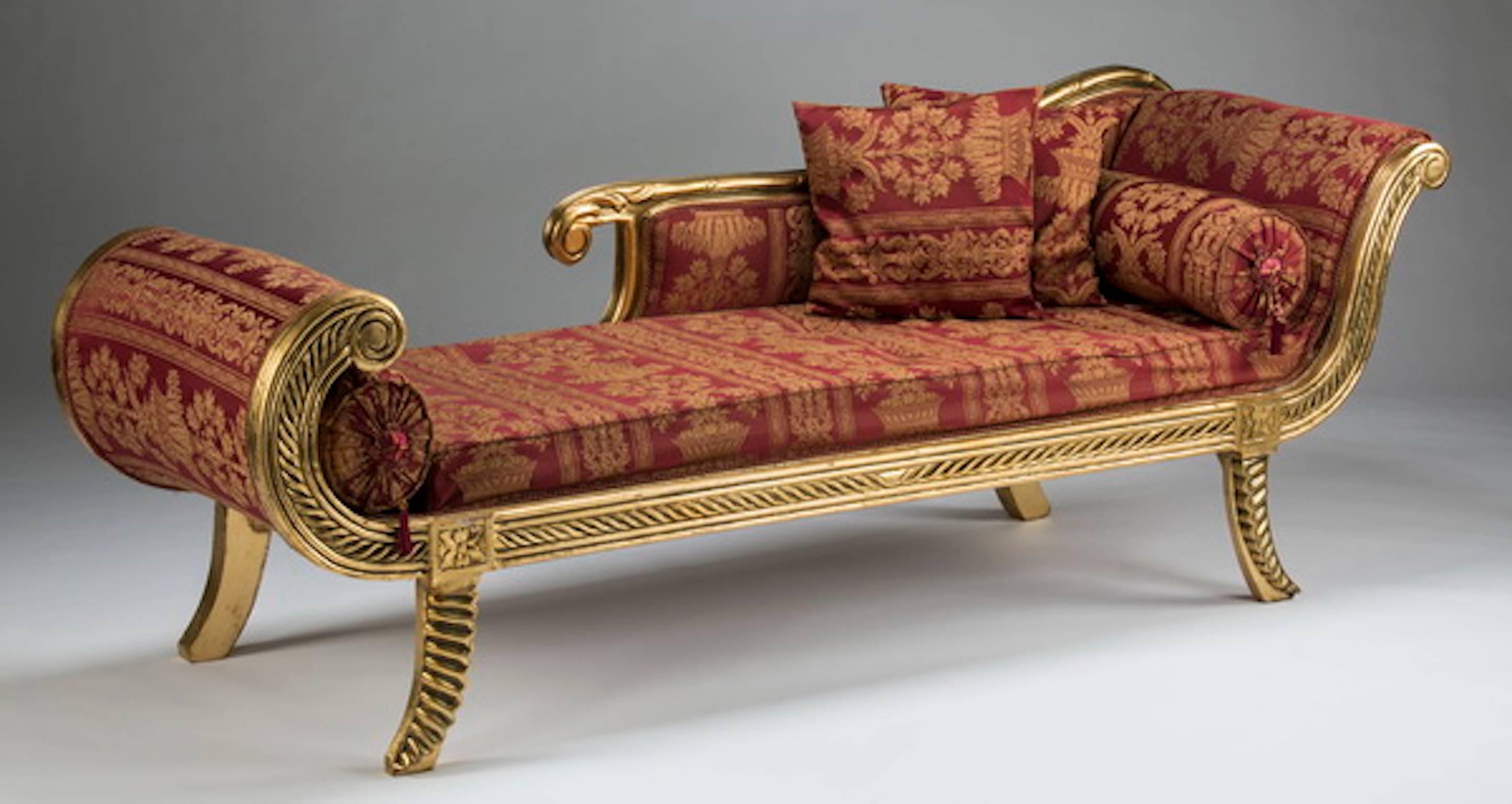 Empire style carved and paint-decorated chaise longue, the reeded hardwood frame upholstered in pink floral embroidered jacquard with associated bolsters and throw pillows, the whole rising on four out swept feet. Measures: 27