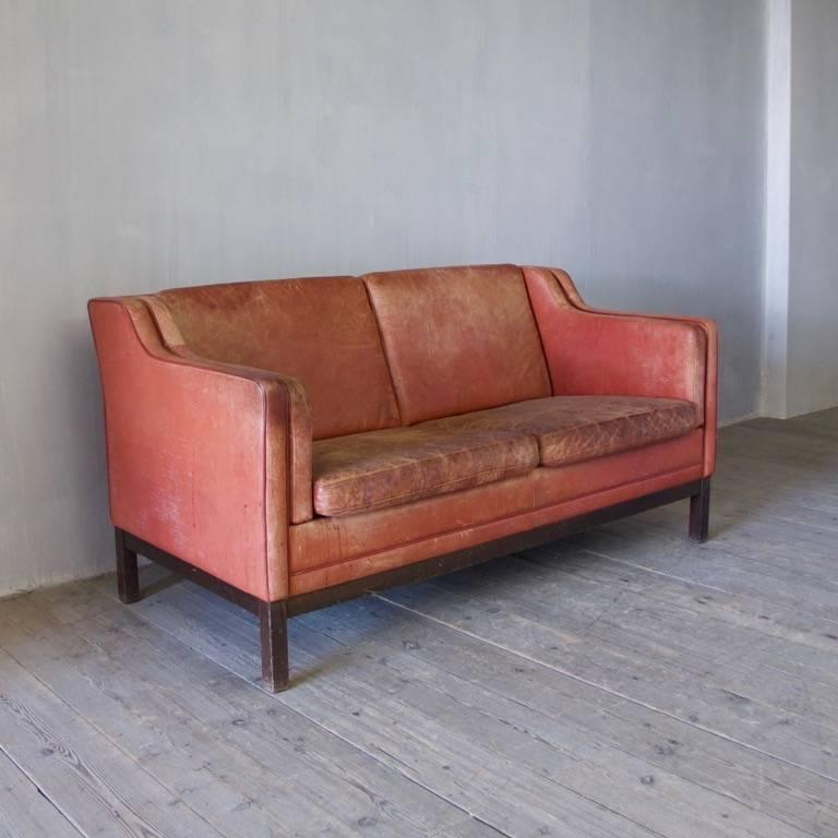 A great mid-20th century sofa, in the style of Børge Mogensen in original red leather upholstery. One small patch to the front of one cushion.