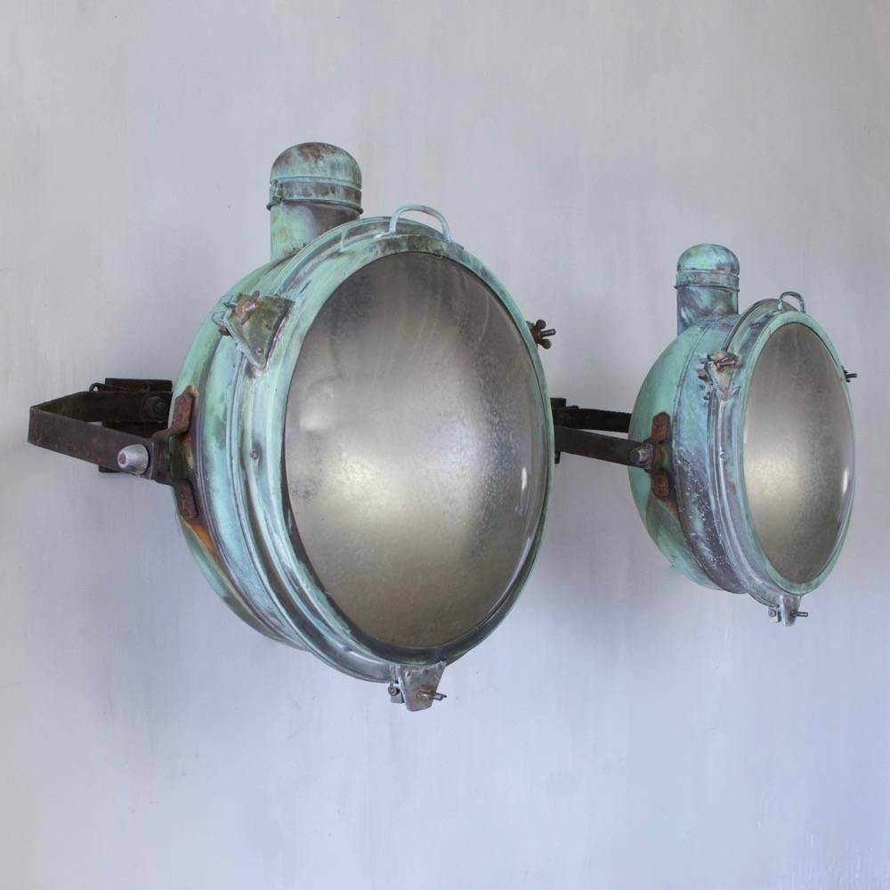 A very large pair of copper searchlights with iron mounting brackets and original verdigris patination. The original glass shades stamped Holophane, England, circa 1920. Rewired with external flex.