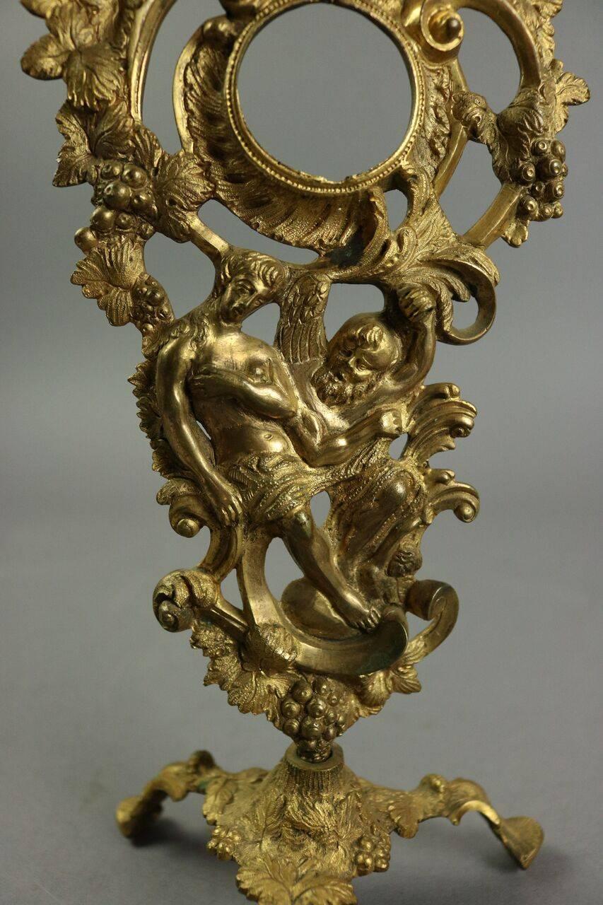 Antique French Rococo gilt bronze figural watch display frame features an intertwined man and woman surrounded by foliate vines and grapes with a 1.5" diameter watch opening, all resting on tripod base, circa 1880.