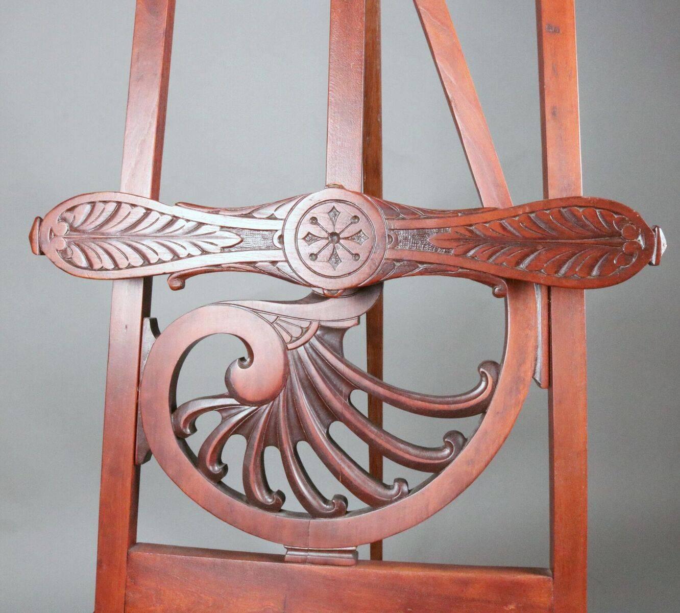 Antique Victorian Eastlake style easel features carved mahogany stylized treble cleft back design terminating in Nautilus scrolls, foliate carved tray and stick and ball literature portfolio, circa 1880.