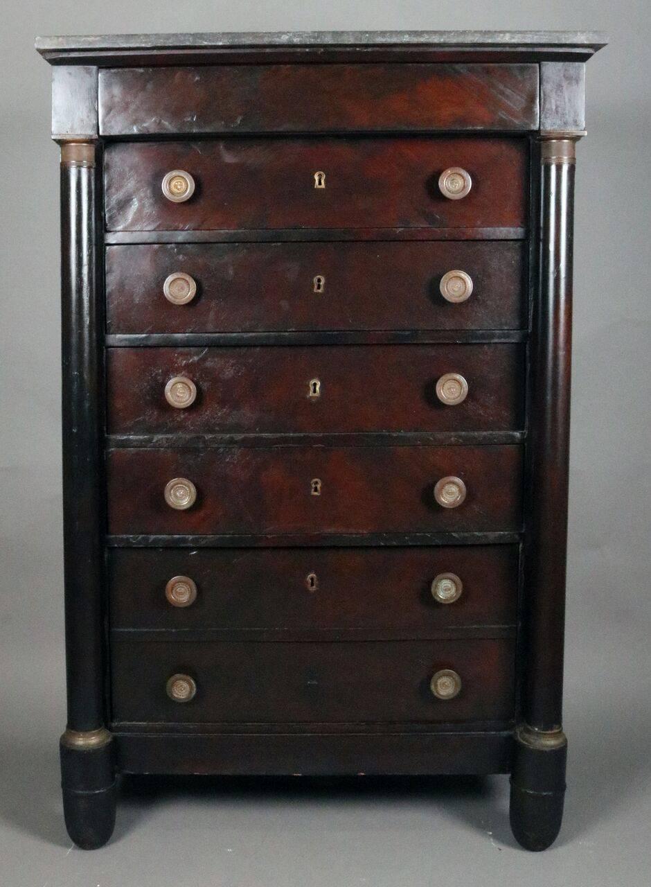 19th Century French Empire tall chest features mahogany construction, seven drawers, flanking full columns with ormolu capitals, figural sunburst brass pulls, bronze mounts, and marble-top.