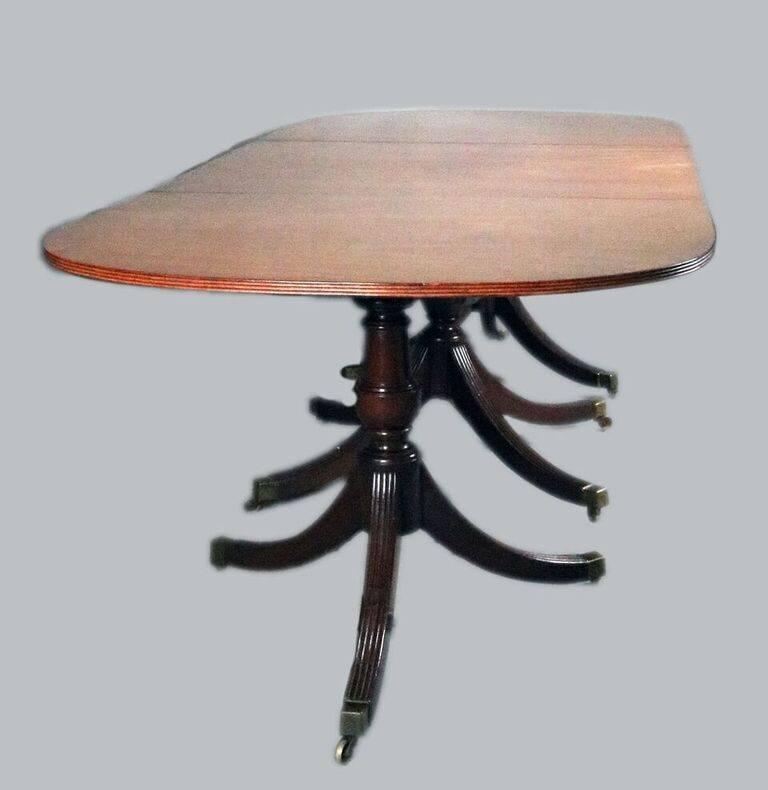 Antique English George III period triple pedestal mahogany dining table features three tilt-top sections, two leaves and Duncan Phyfe style legs terminating in bronze casters, circa 1800.

Measures: 140"long with leaves; 96" long without
