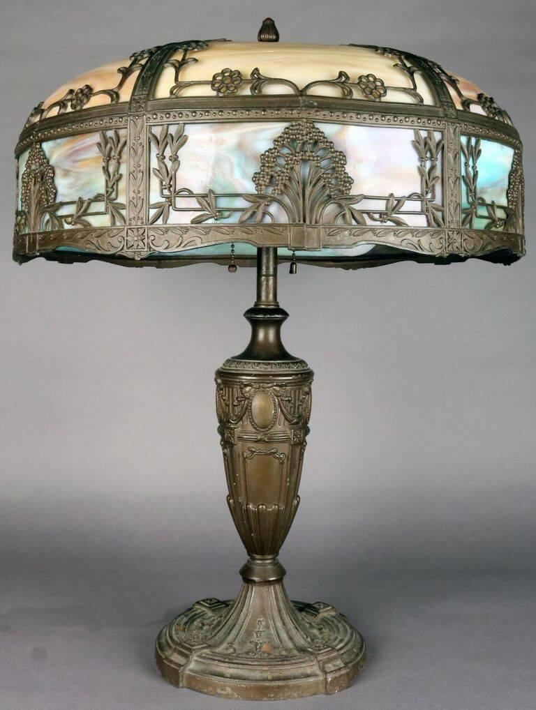 Antique Art Nouveau table lamp features cast base with eight panel foliate filigree two-toned nine caramel on top and blue and pink and purple on bottom band) slag glass shade, circa 1910.
