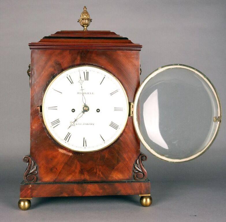 Antique English Georgian Haskell bracket clock features mahogany case with bronze mounts including pineapple finial and lion head handles, "Haskell" and "Salisbury" on clock face, circa 1815. Clock is in working condition and