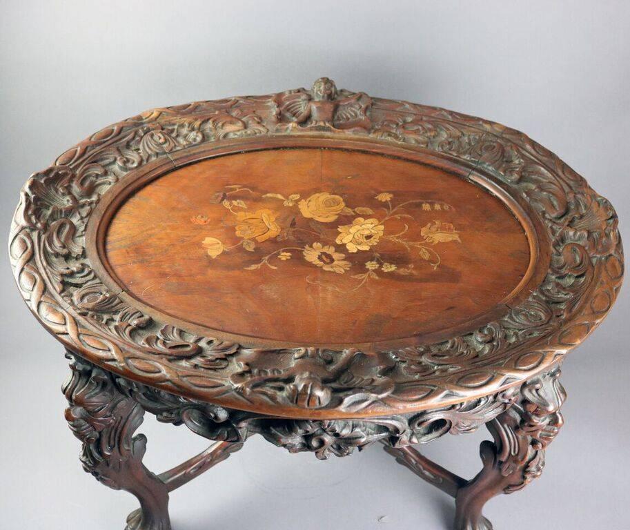 Antique figural Continental tea table features heavily caved foliate border and skirt, legs beginning in lion heads and terminating in paw feet, floral inlaid top with removable glass tray, circa 1900.