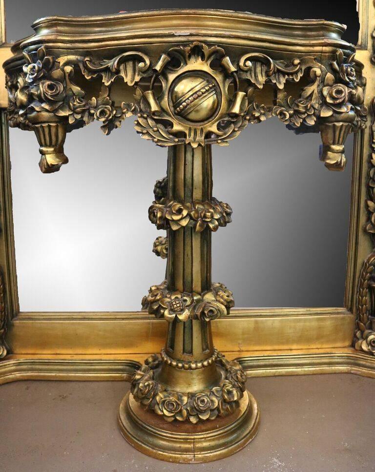 Oversized French Baroque style pier hall mirror features giltwood frame with crown and shield crest flanked by floral garland, castings of reeded columns enhanced with floral garland and attached marble top Stand with pieced floral apron and floral