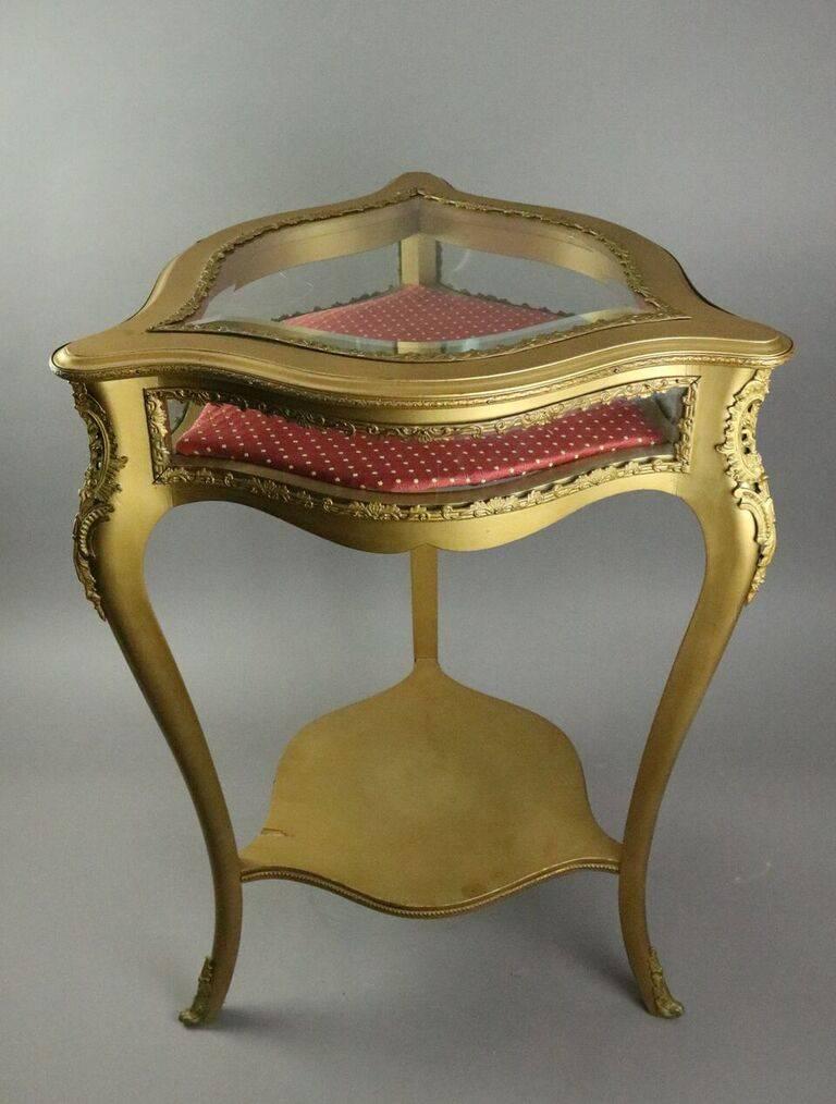 Antique French Louis XV style curio occasional table features giltwood triangular napkin fold construction with serpentine sides and traditional cabriole legs with applied decoration, lined display case with curved glass sides, and hinged top with