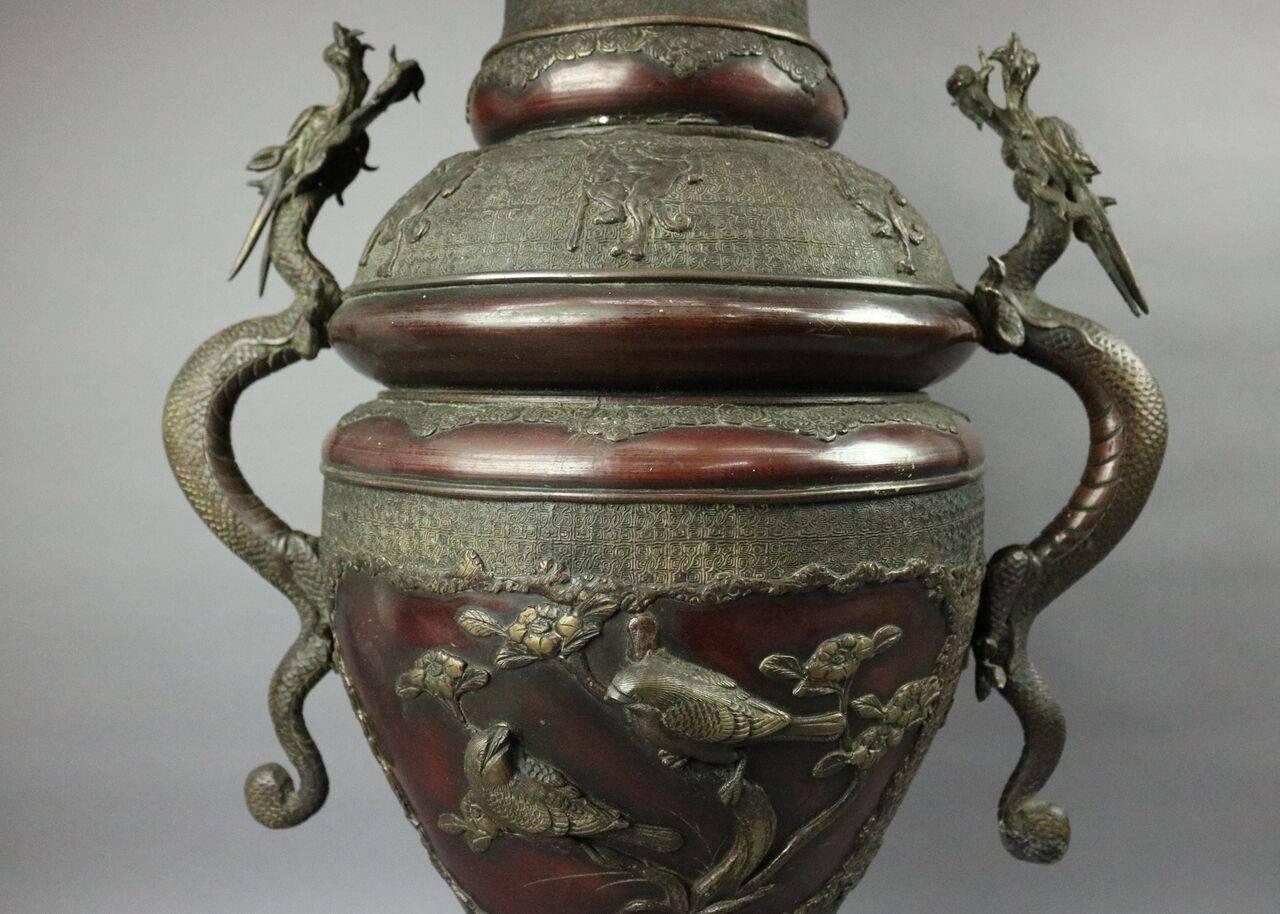 Antique Japanese Meiji period figural open floor urn (vase) features scalloped shaped opening atop intricately decorated neck on a body decorated in relief of floral and aviary figures flanked by applied double handles of stylized full body dragons,