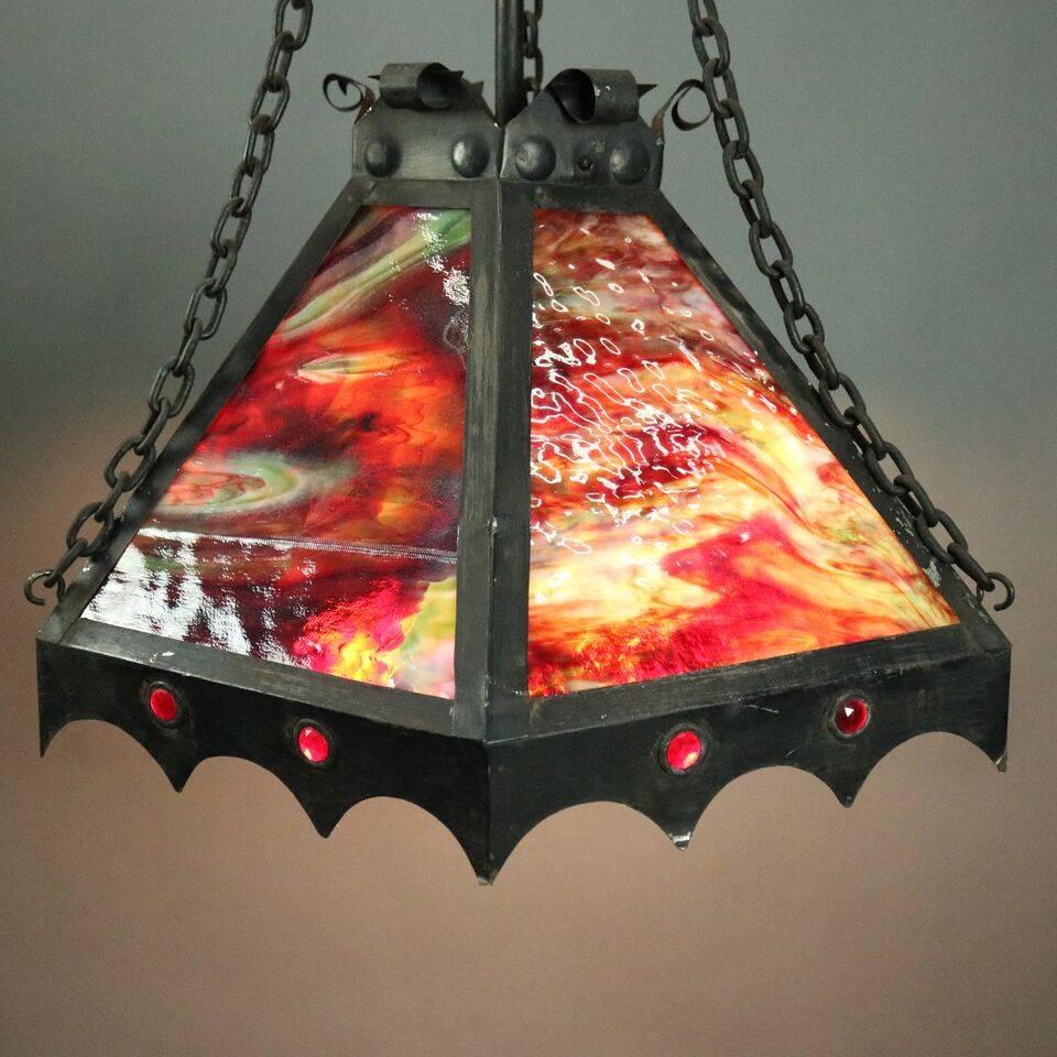 Antique Arts & Crafts six-panel slag glass hanging light features slag glass in green, amber and red with red jeweled insets in apron, three independently controlled bulbs in a black painted tin frame, newly re-wired, circa 1910

Measures: 43