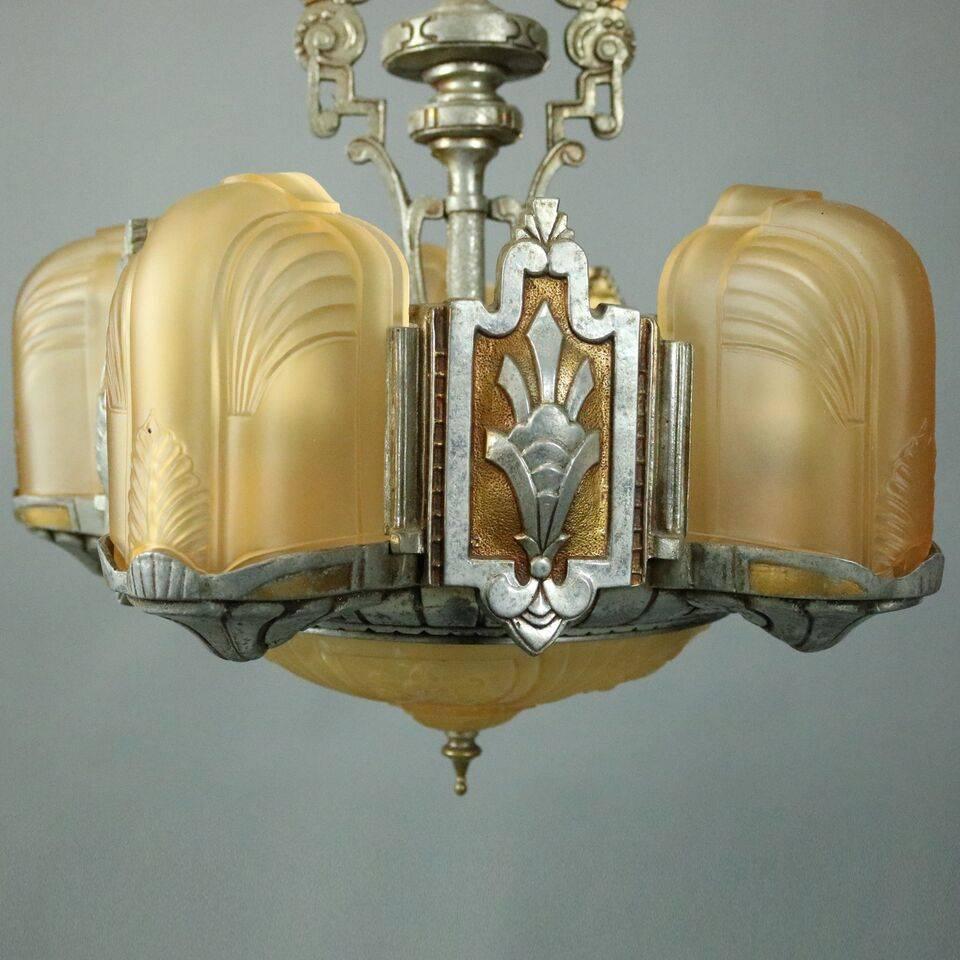 Antique French Art Deco chandelier features five lights plus a center light ornamented with frosted amber gadrooned shades in a cast metal geometric frame alternating with medallions of fleur de lis accents finishing with a gadrooned shade attached