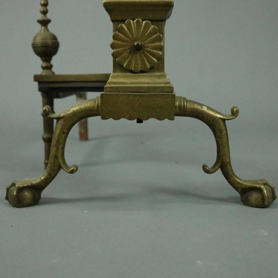 Antique pair of Federal style brass andirons feature urn and flame finials above a torchiere body and arched legs accented at the knee and heel with scrolls and terminating in claw and ball feet connected to finial topped firedogs, circa
