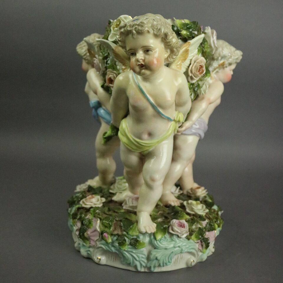 Antique German figural Meissen Schierholz hand-painted porcelain compote features three cherubs supporting floral decorated compote, underglaze mark on base, 19th century.

Measures: 13" high x 11"diameter.