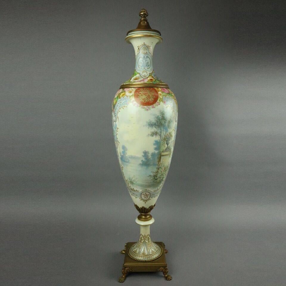 19th century large French Sèvres porcelain urn features hand-painted floral, cherub and goddess frontal scene with lake and landscape scene en verso with bronze lid and base, artist signed L. Bertren, a well recognized Sèvres decorator.

Measures: