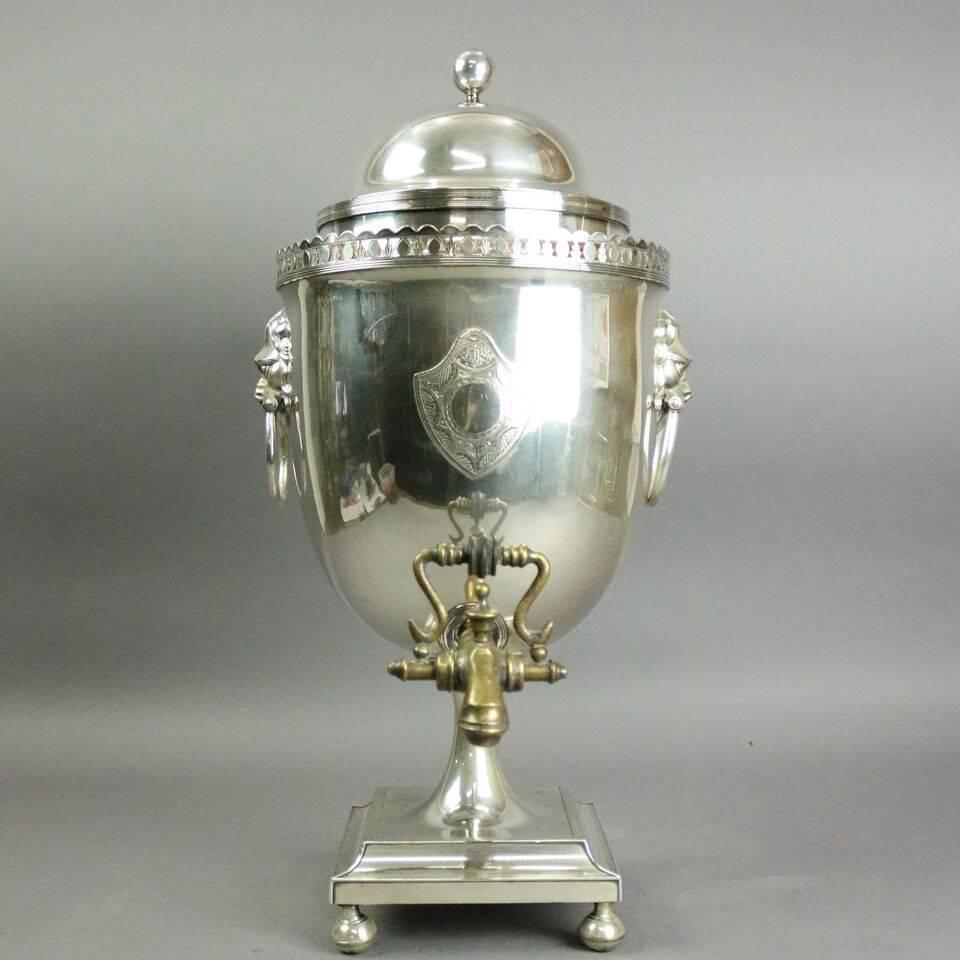 Antique English Regency silver plate samover (tea urn) features double lion head handles, applied shield on urn face, scalloped gallery, bronze outlet spout sitting atop narrow pedestal on footed base, early 19th century.

Measures: 21"