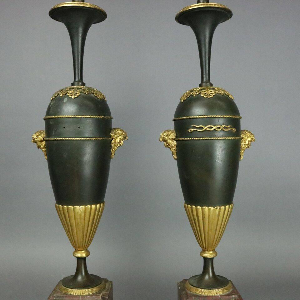 Pair of antique Classical bronze parcel-gilt marble lamps feature urn shaped base with double handles of figural satyr masks and central intertwined serpents, seated on square marble plinth, newly re-wired, circa 1900.
