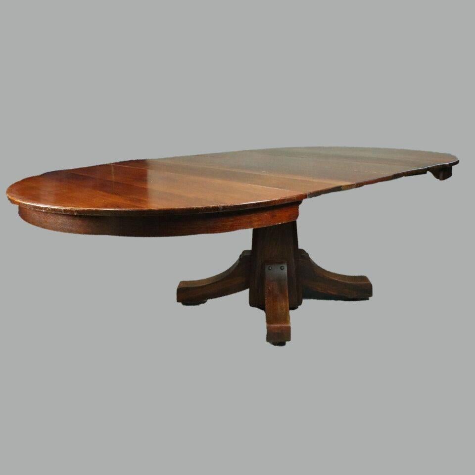 Antique Stickley brothers Arts and Crafts mission oak dining table features traditional Arts and Crafts design of simple functionality with central tapered square pedestal terminating in four sweeping corbel legs, round table expanding to large oval