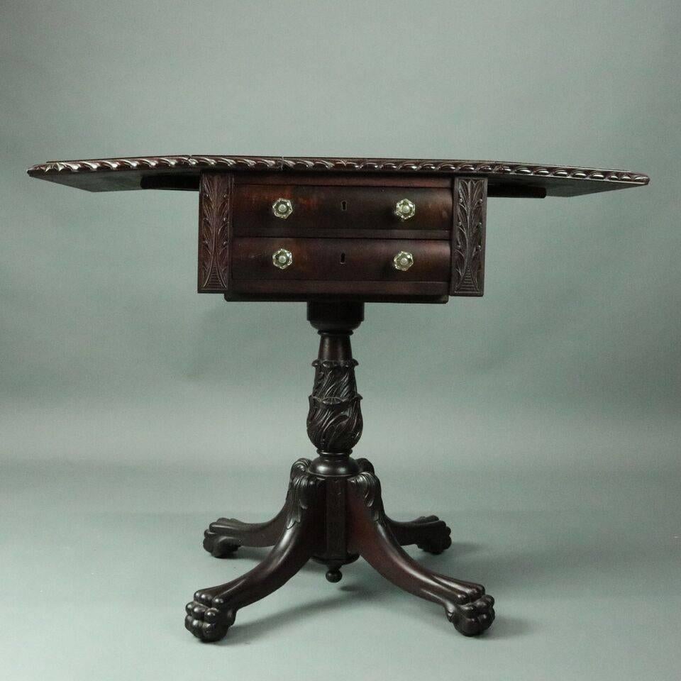 Antique American Empire stand features mahogany construction with two bowed drawers flanked by incised foliate design, drop-leaf top with carved twisted rope border atop two-drawer case supported by carved acanthus leaf shaft on plinth terminating