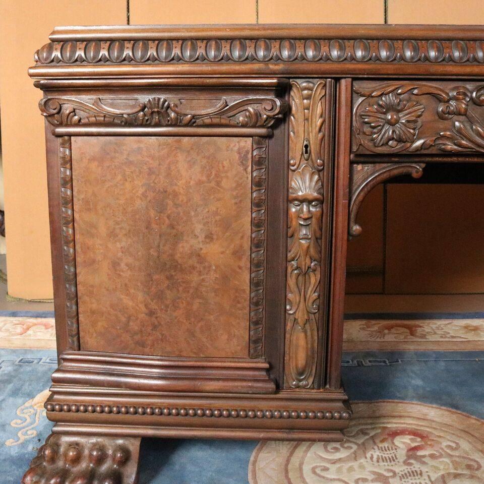 Massive antique Baroque German heavily carved desk features walnut construction with molded egg and dart fore-edge with central carved drawer with carved foliate and scroll design flanked by burl walnut panelled doors with carved panels of mask and