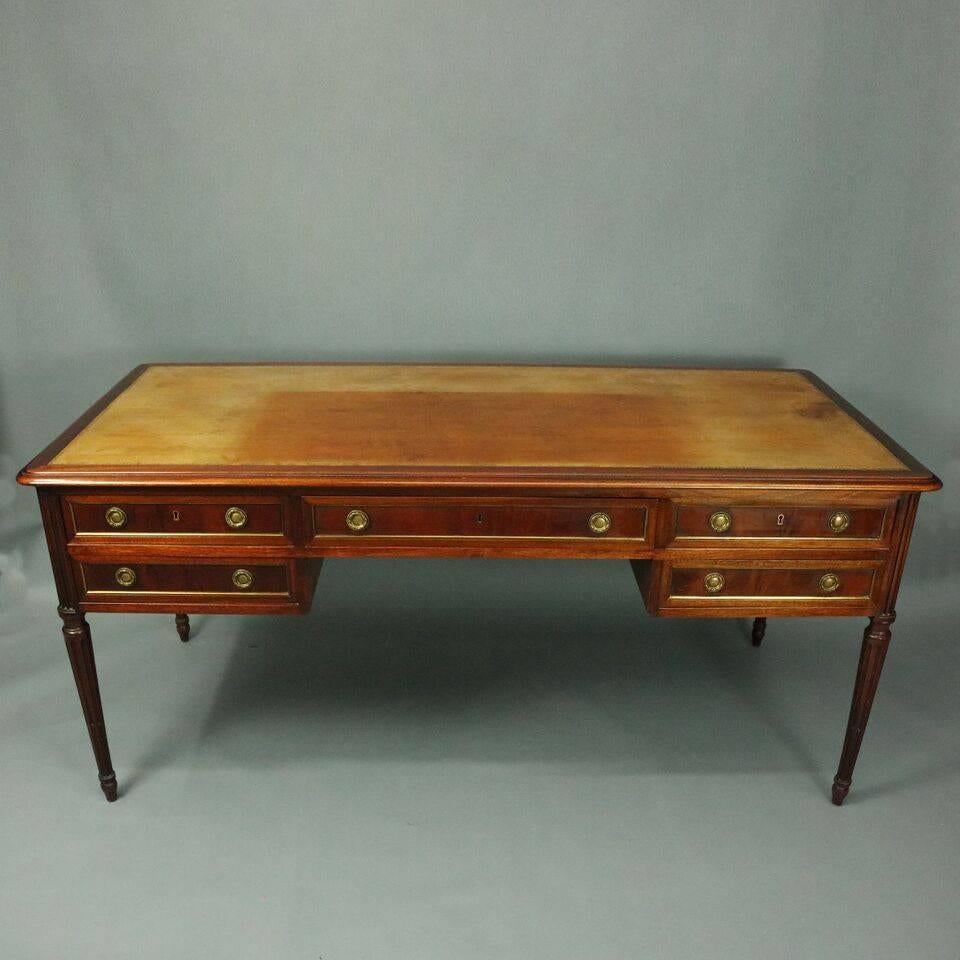 Antique English Sheraton writing desk features mahogany construction including large leather writing surface with two pull-out extensions, larger central locking drawer flanked by smaller drawers with bronze banding and pulls, case seated atop