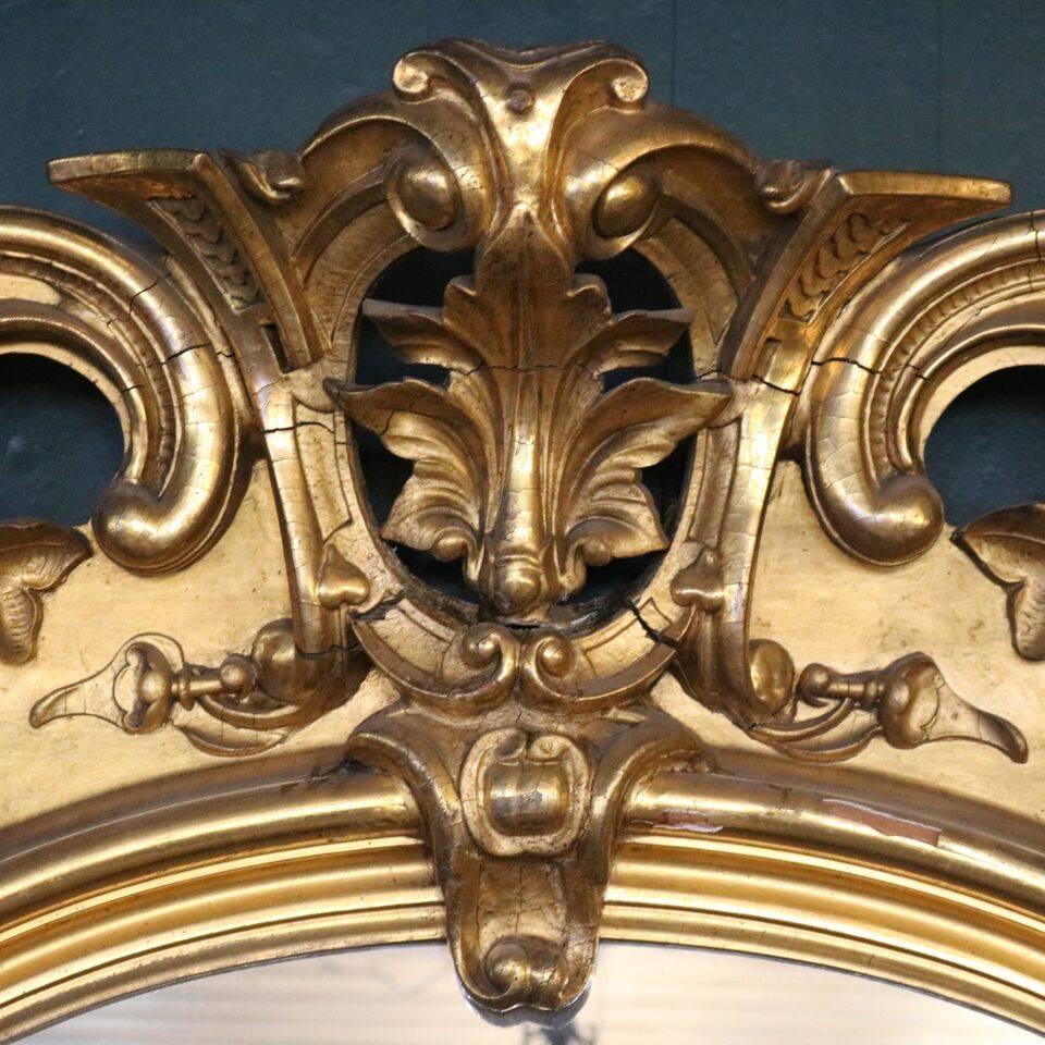 Oversized antique French Rococo pier mirror features first finish gold gilt surround of foliate and scroll decoration including a crest of volutes affrontes with central palmette. Mirror is seated on gold gilt marble top base with pierced foliate