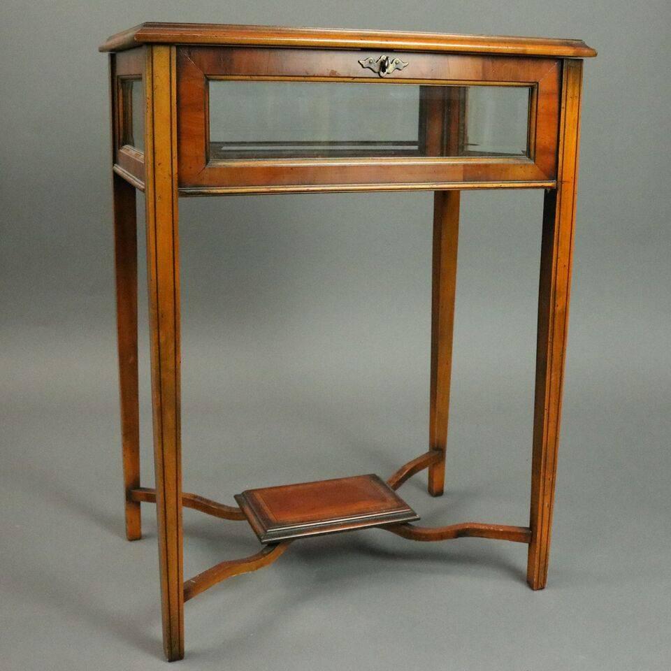 Antique English School mahogany vitrine stand features satinwood inlay, ebonized banding, tapered legs, stretchers terminating in central display platform, beveled glass panels and locking case with 2 keys, circa 1900.

Measures - 30" H x