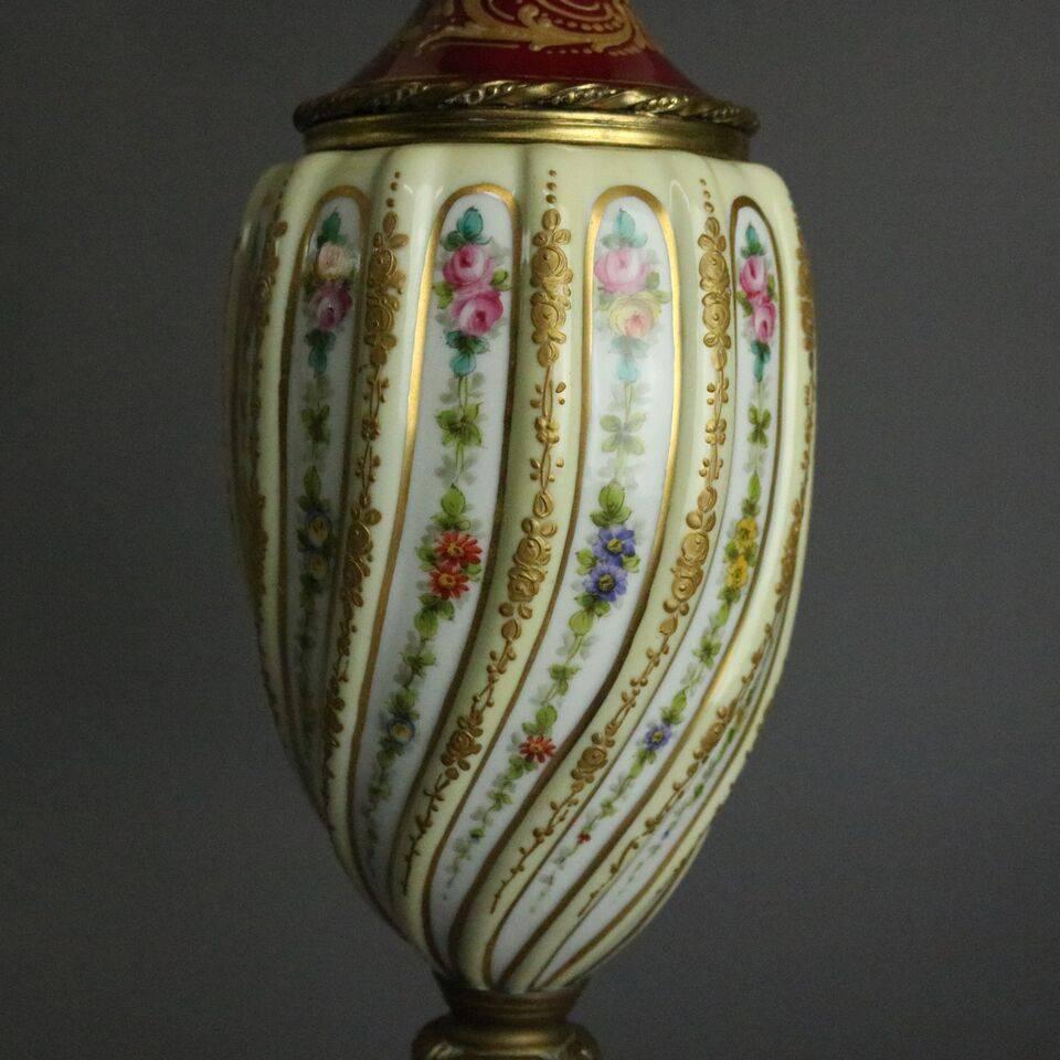 Pair of antique Sèvres table lamps feature hand-painted floral and gold gilt twisted urn bodies seated on and topped with gilt decorated red necks and columns atop bronze bases, circa 1890.

Measures: 32" H x 5"sq (base), shades