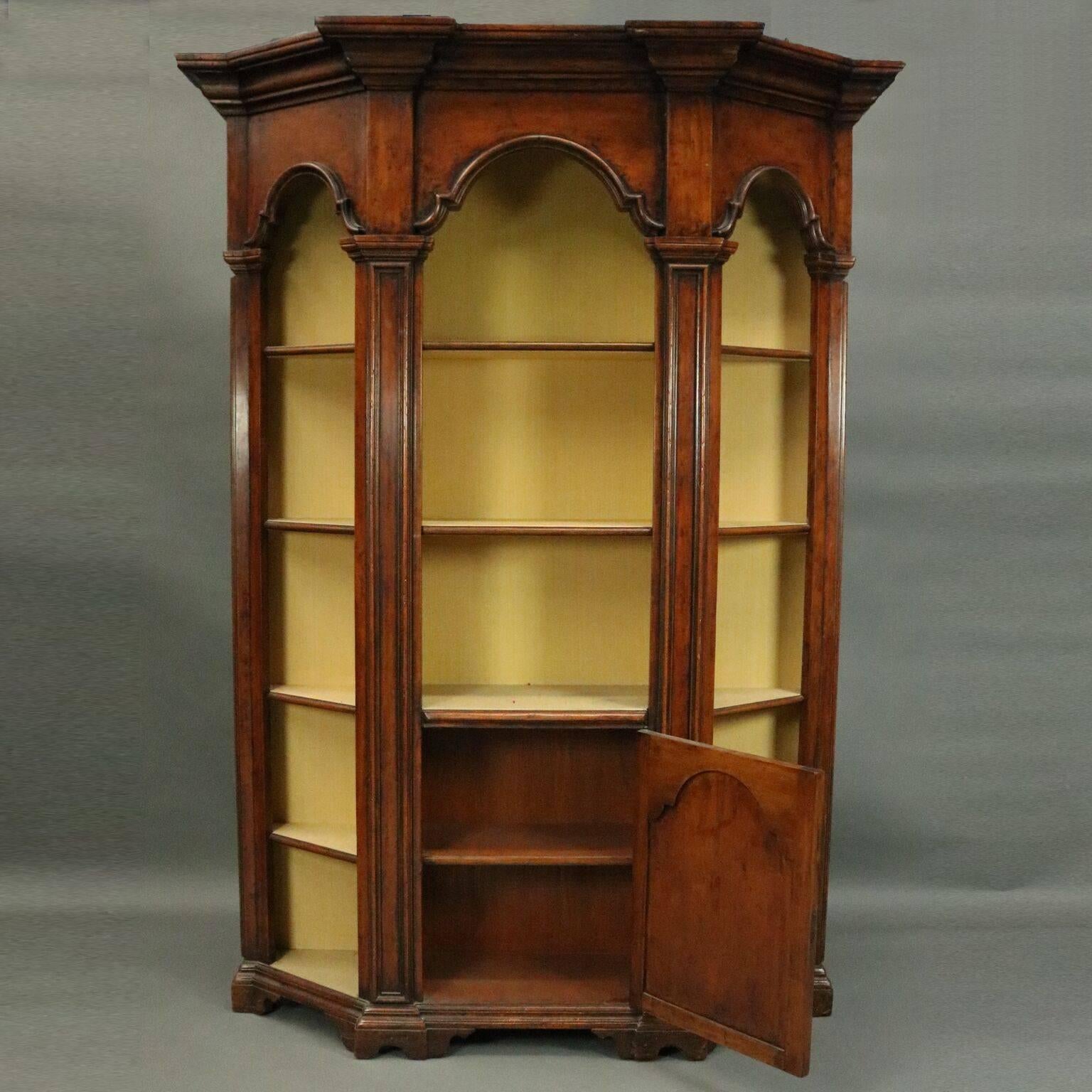 Antique architectural Italian mahogany faceted bookcase features three sides framed with columns and arched displays, five shelves on each side with two on the front behind a blind door, fabric lined, mid-20th century.

Measures - 88.5