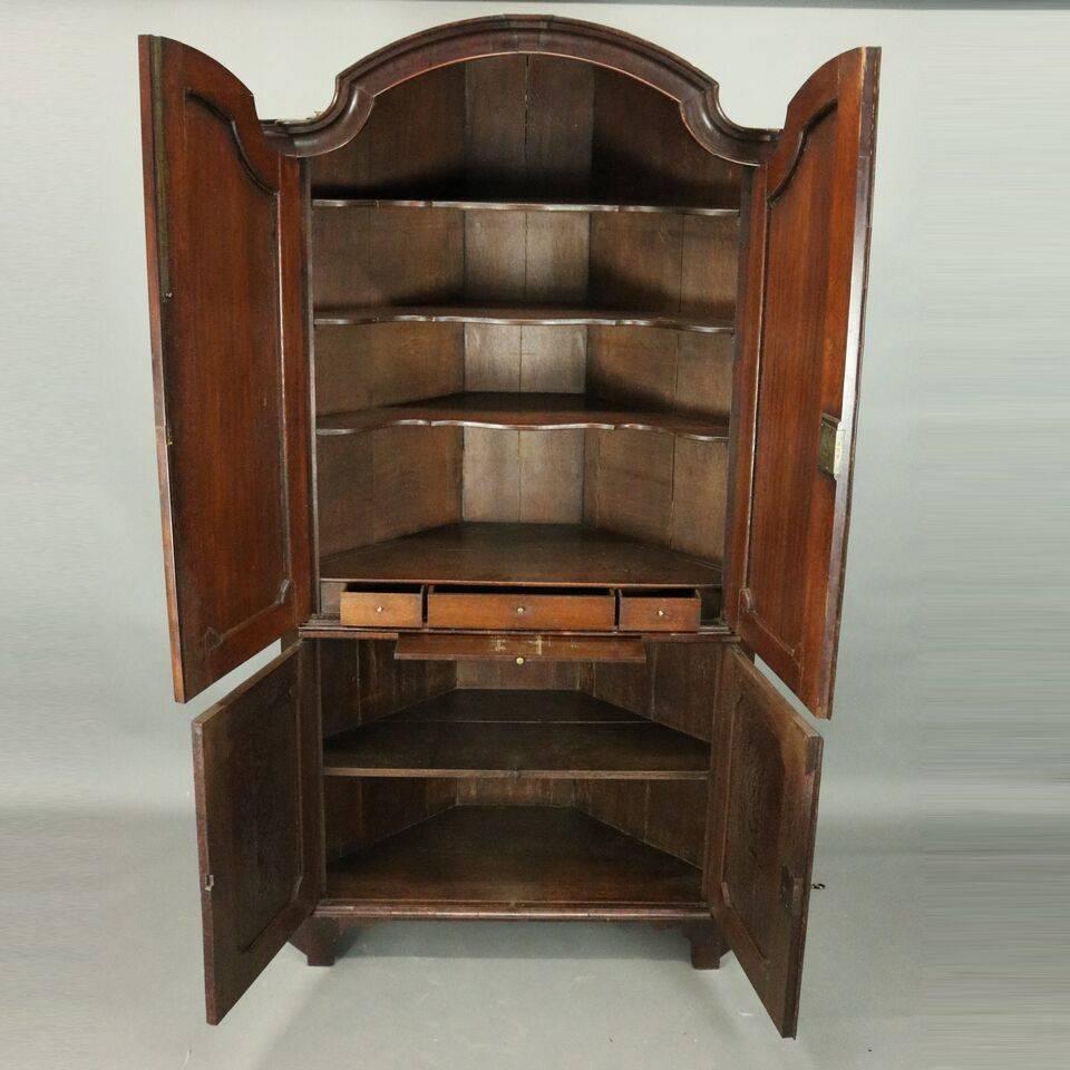Antique English two-piece Renaissance Revival walnut corner cupboard features double arched doors with reserves on upper opening to reveal shelved compartment with drawers and pull-out work surface, lower double doors also with reserves open to