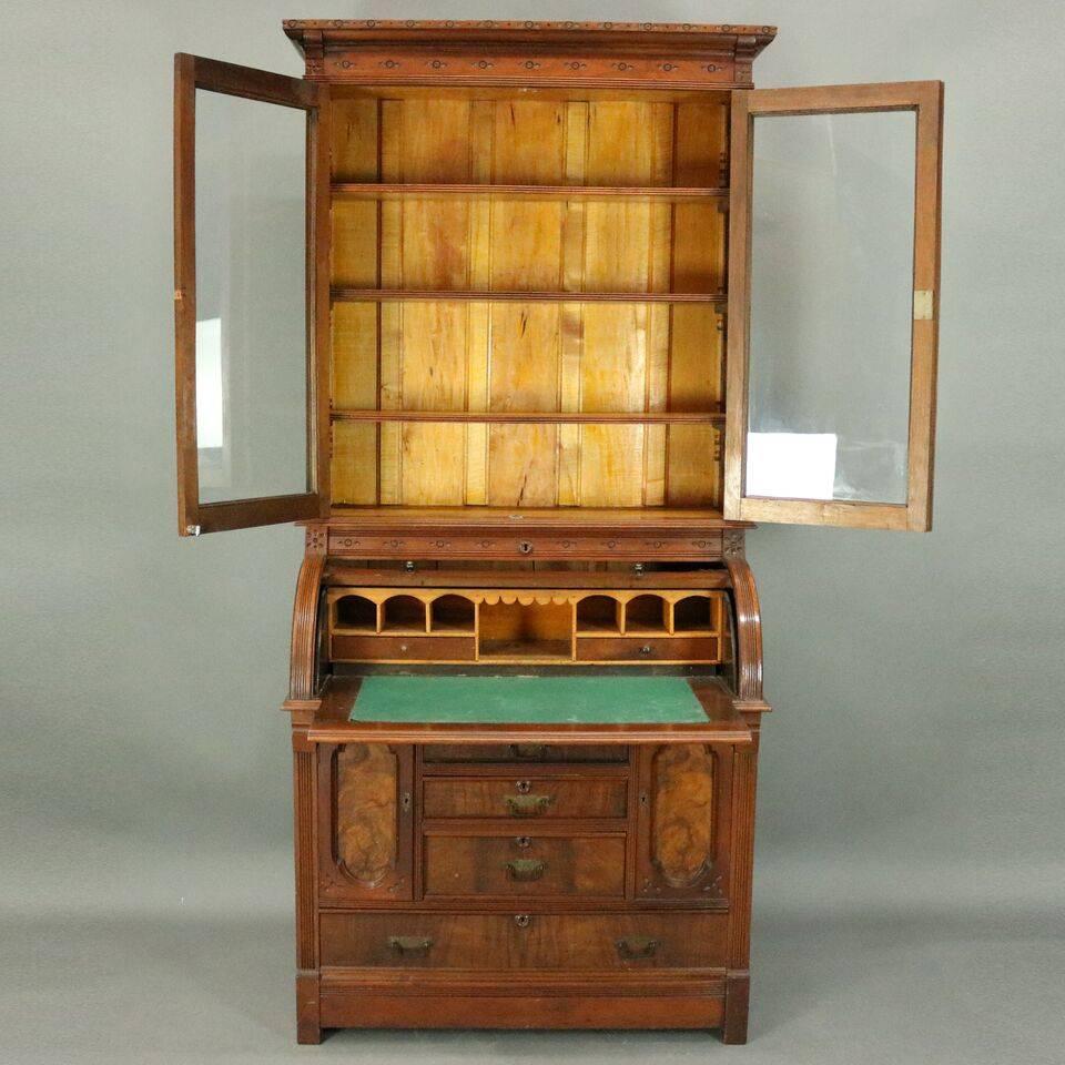 Antique Eastlake cylinder secretary features burl walnut construction including cylinder desk opening to pull-out writing surface with interior pigeon holes and drawers above storage compartments and drawers and below double glass door bookshelves,