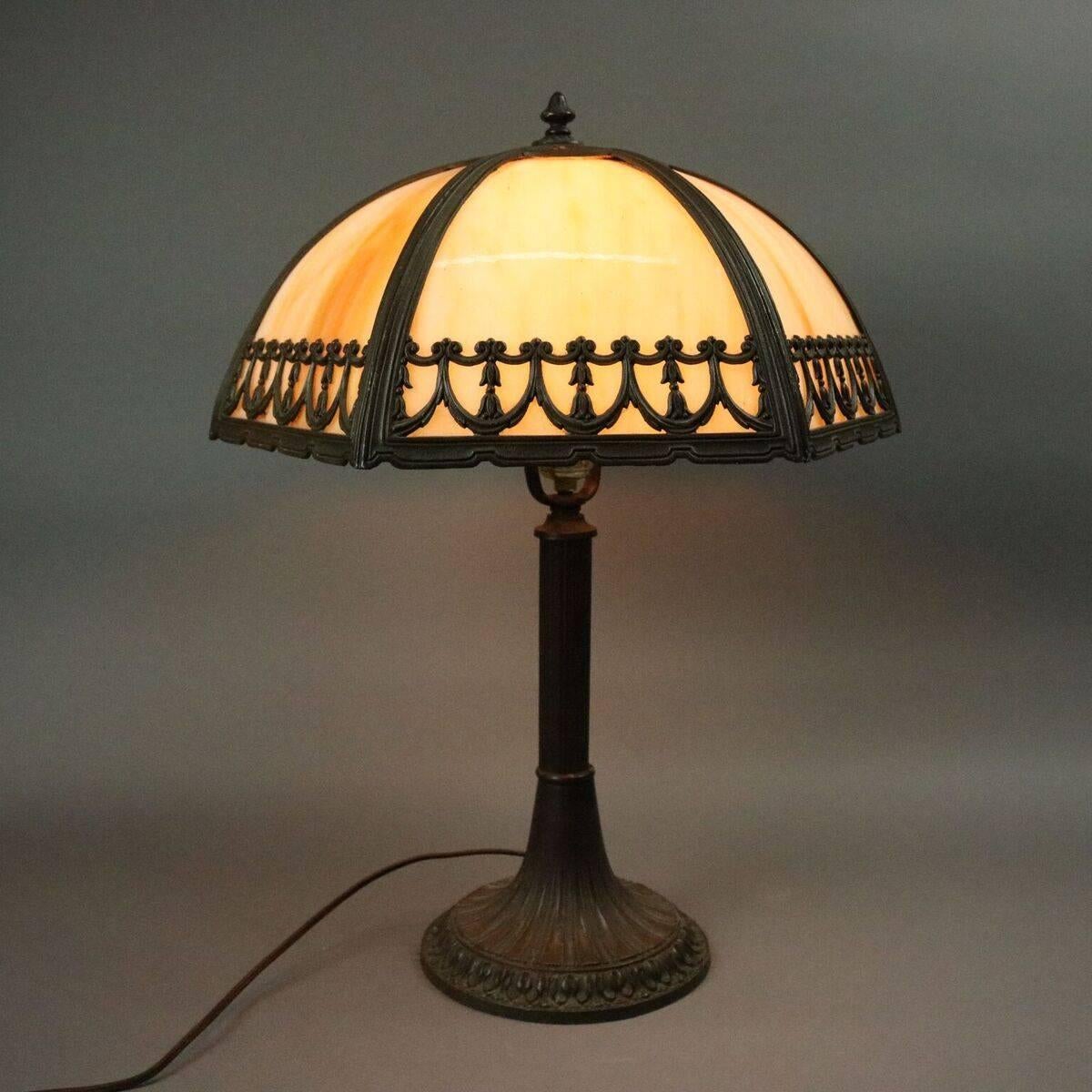 Antique Arts and Crafts table lamp by Bradley and Hubbard features six cream/caramel slag glass panels housed in pierced bronze frame with swags and bellflowers supported by gilt bronze base, circa 1920

Measures: 22" H x 17" diameter.