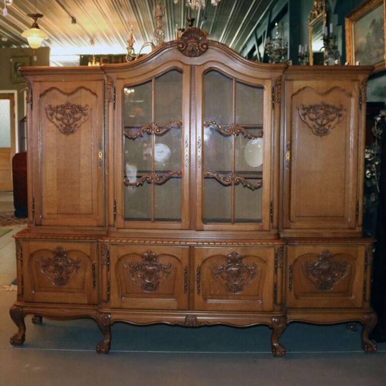 Oversized antique Belgian oak breakfront cabinet features upper cabinet with central double glass doors over shelved display compartment flanked by blind cupboards with carved foliate, c-scroll, and shell design. Lower has four doors with matching