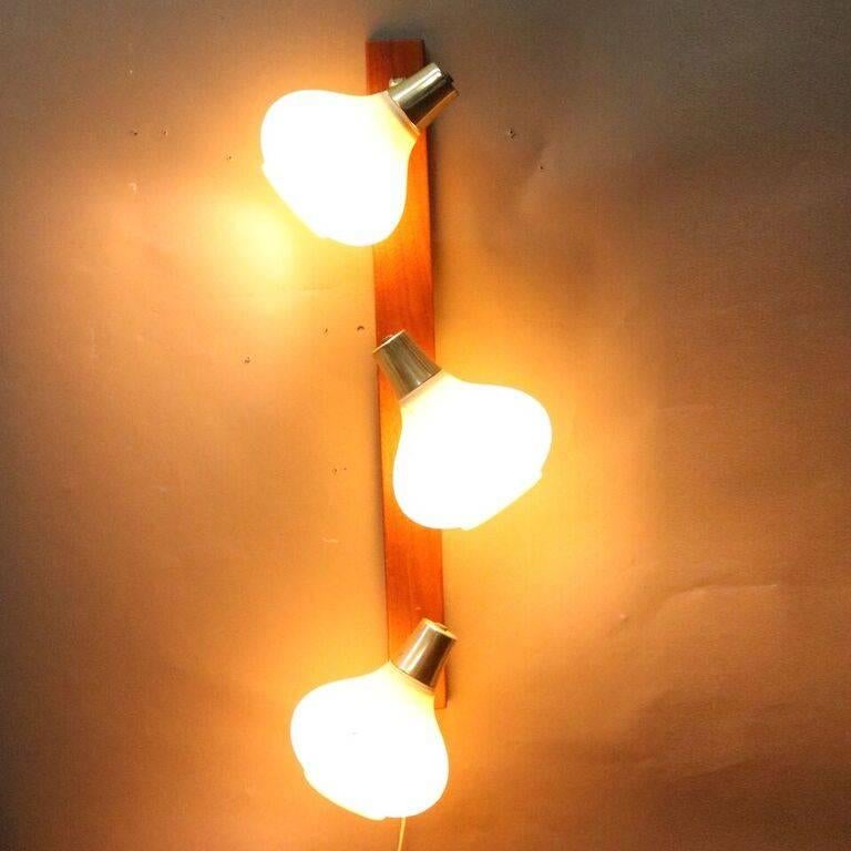 Mid Century Danish Modern wall sconce features teak base with three teardrop-shaped molded ribbed plastic shades, circa 1960

Measures - 13"h x 31"w x 3"d

*Companion wall light listed separately*